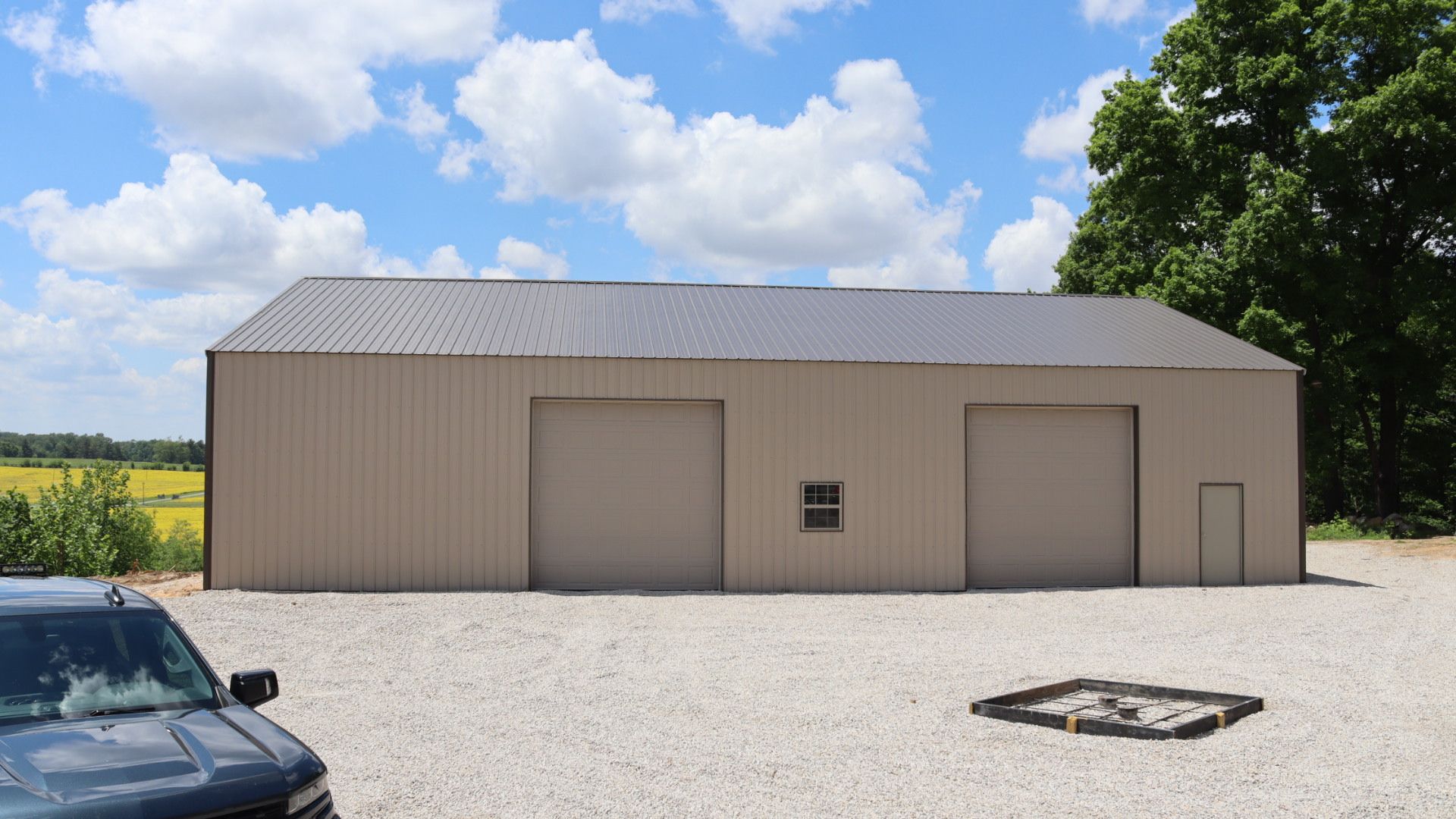 Beige metal building with three garage doors on a gravel lot under a partly cloudy sky
