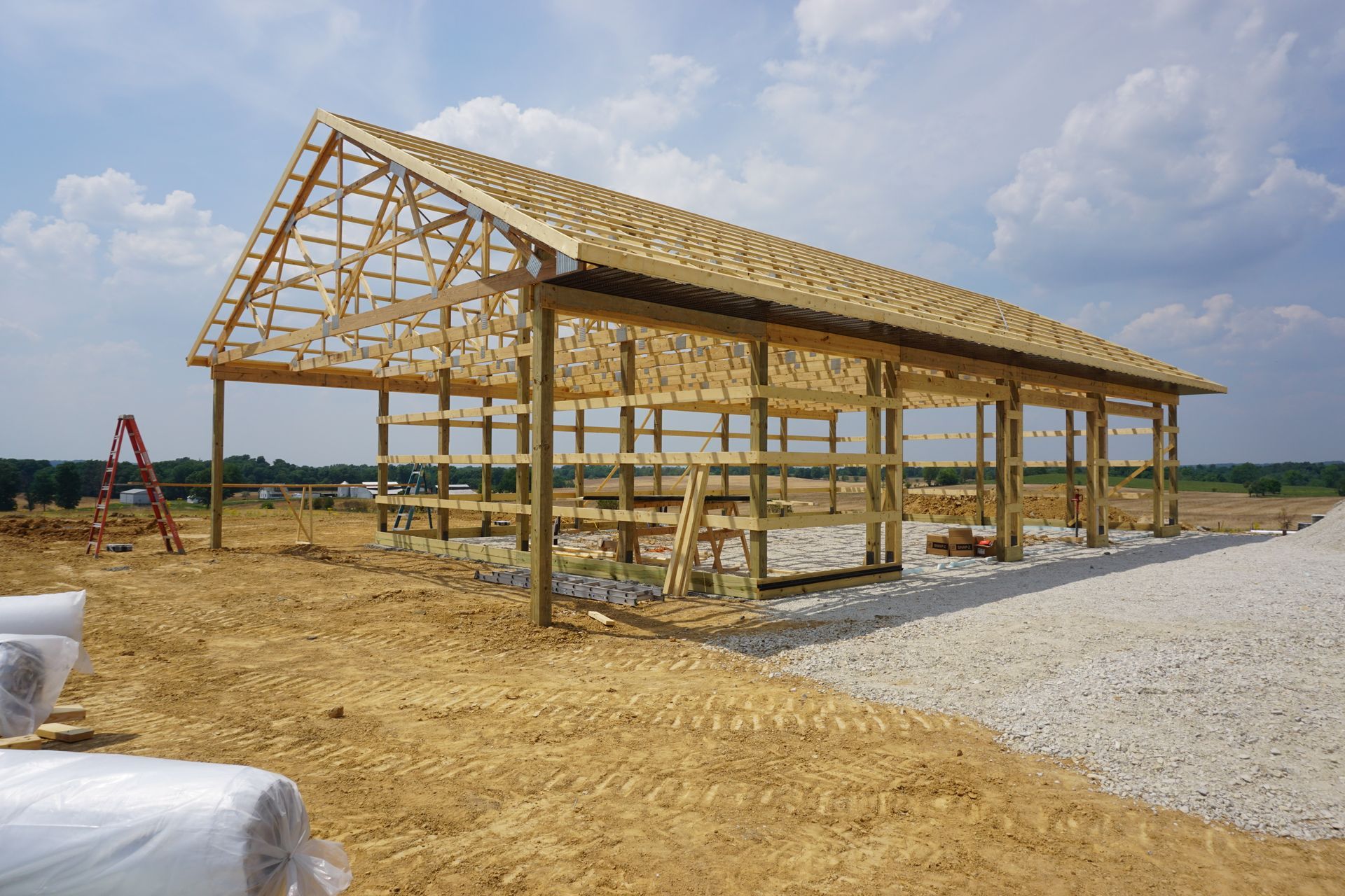 Partially built wooden barn frame on a gravel lot under a cloudy sky