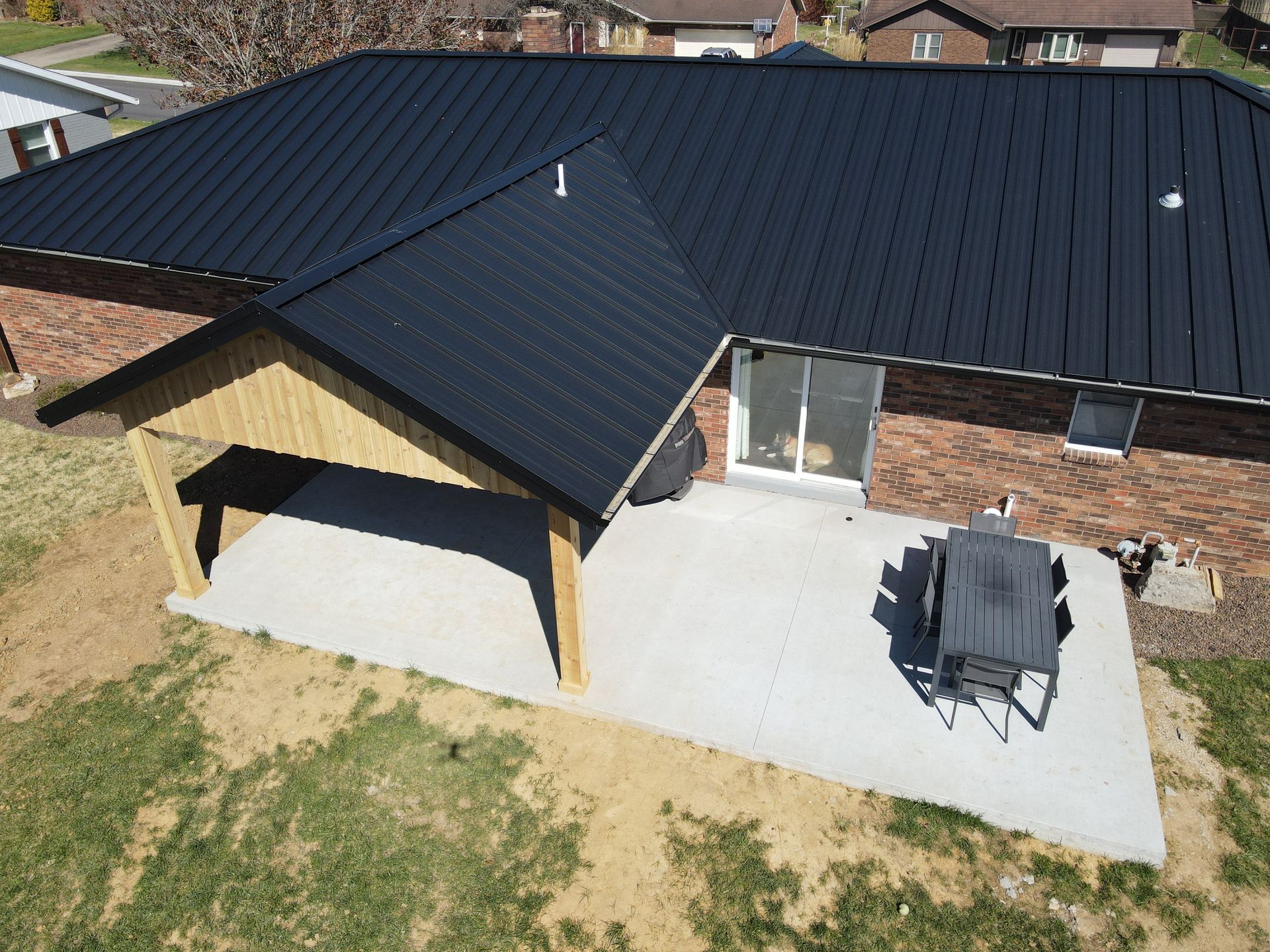Aerial view of a house with a black roof, brick exterior, patio, and yard
