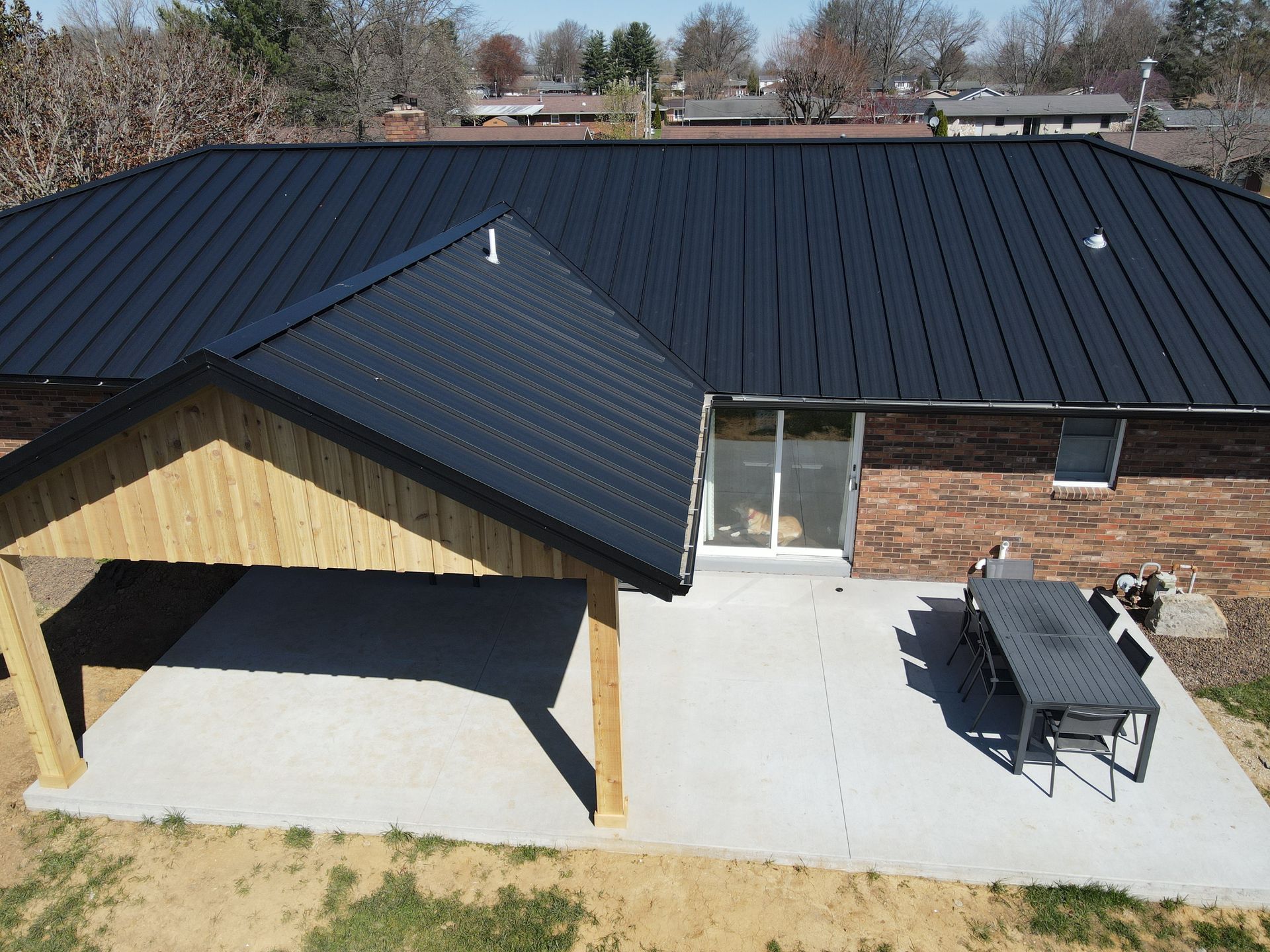 Backyard patio with a dark metal-roofed house, covered porch, and outdoor dining set on a concrete slab