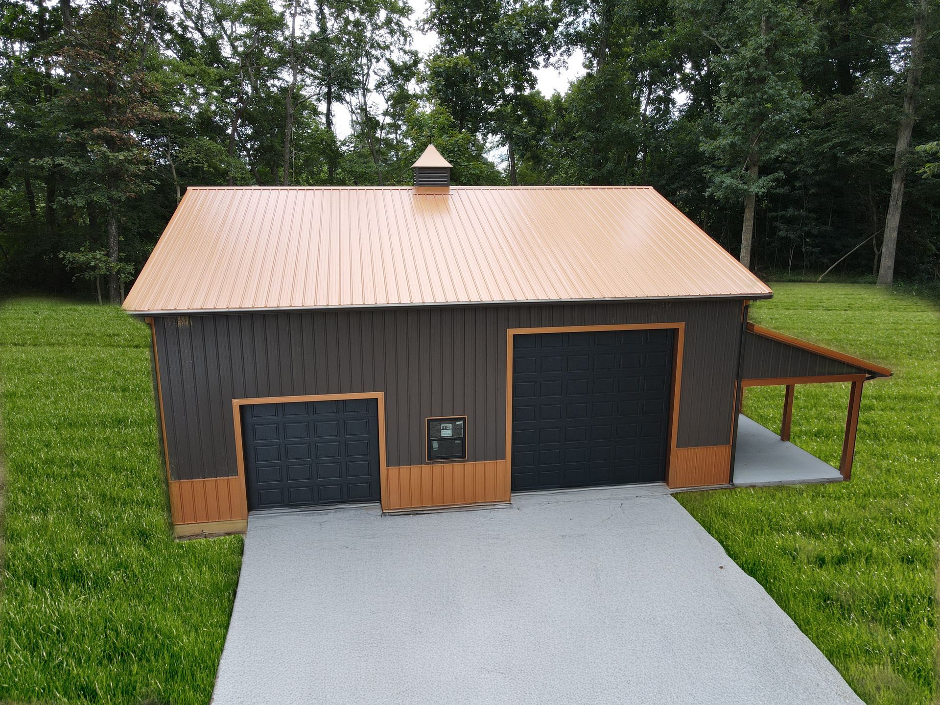 Small gray shed with tan roof, double garage door, and driveway in a grassy yard.