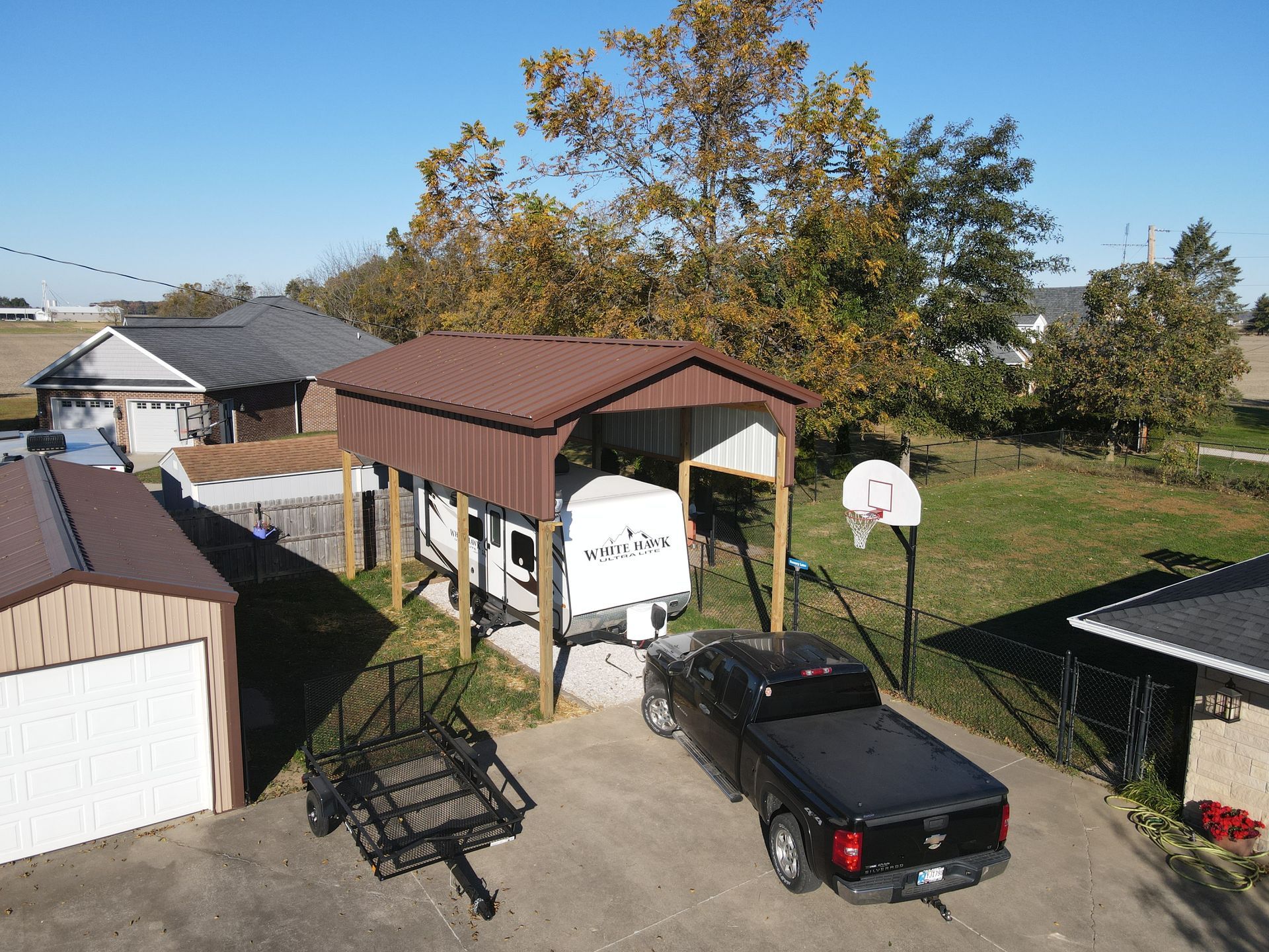 Backyard with detached garage, covered carport, truck, and basketball hoop on a sunny day