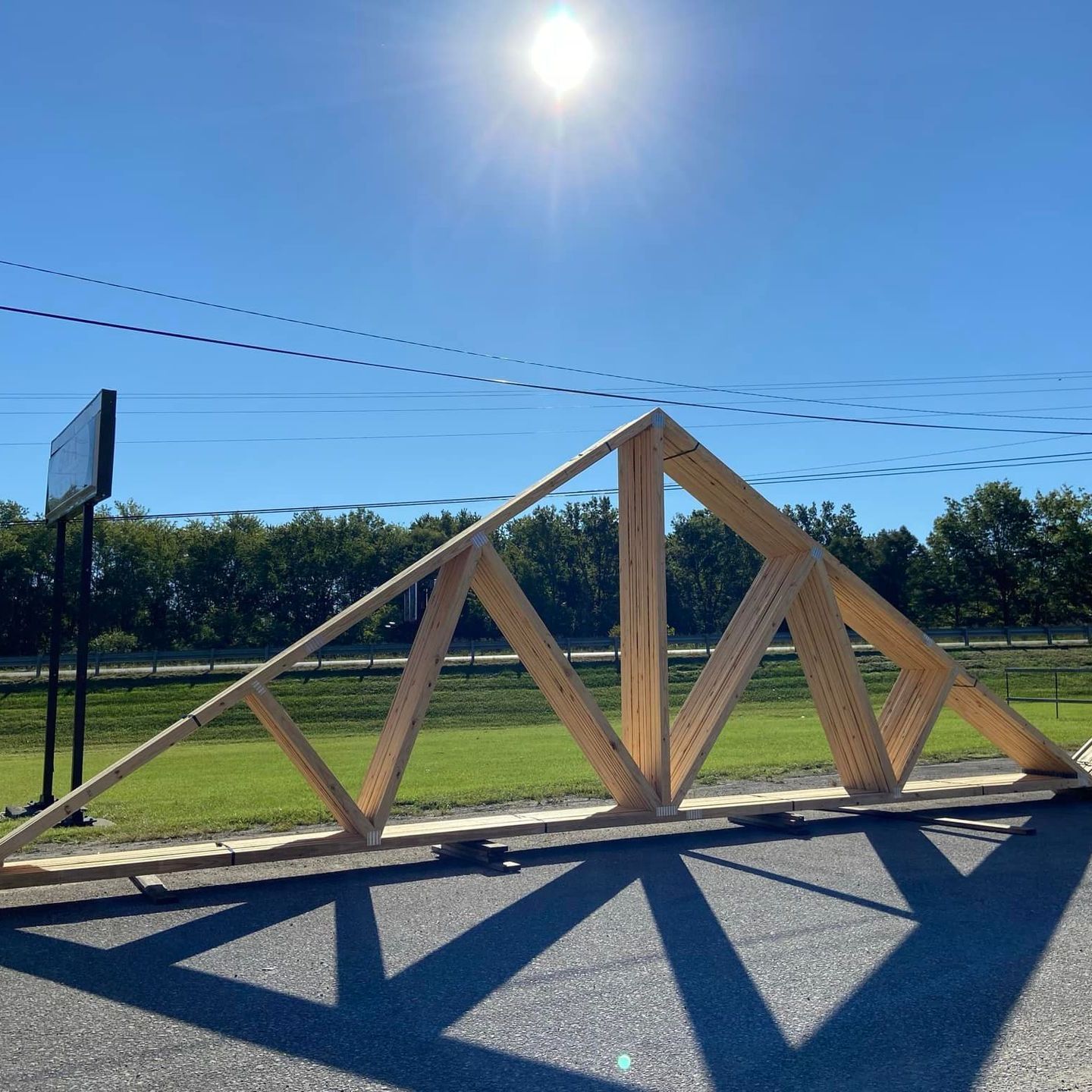 Wooden triangular sculpture on a roadside under a bright blue sky, casting long shadows.
