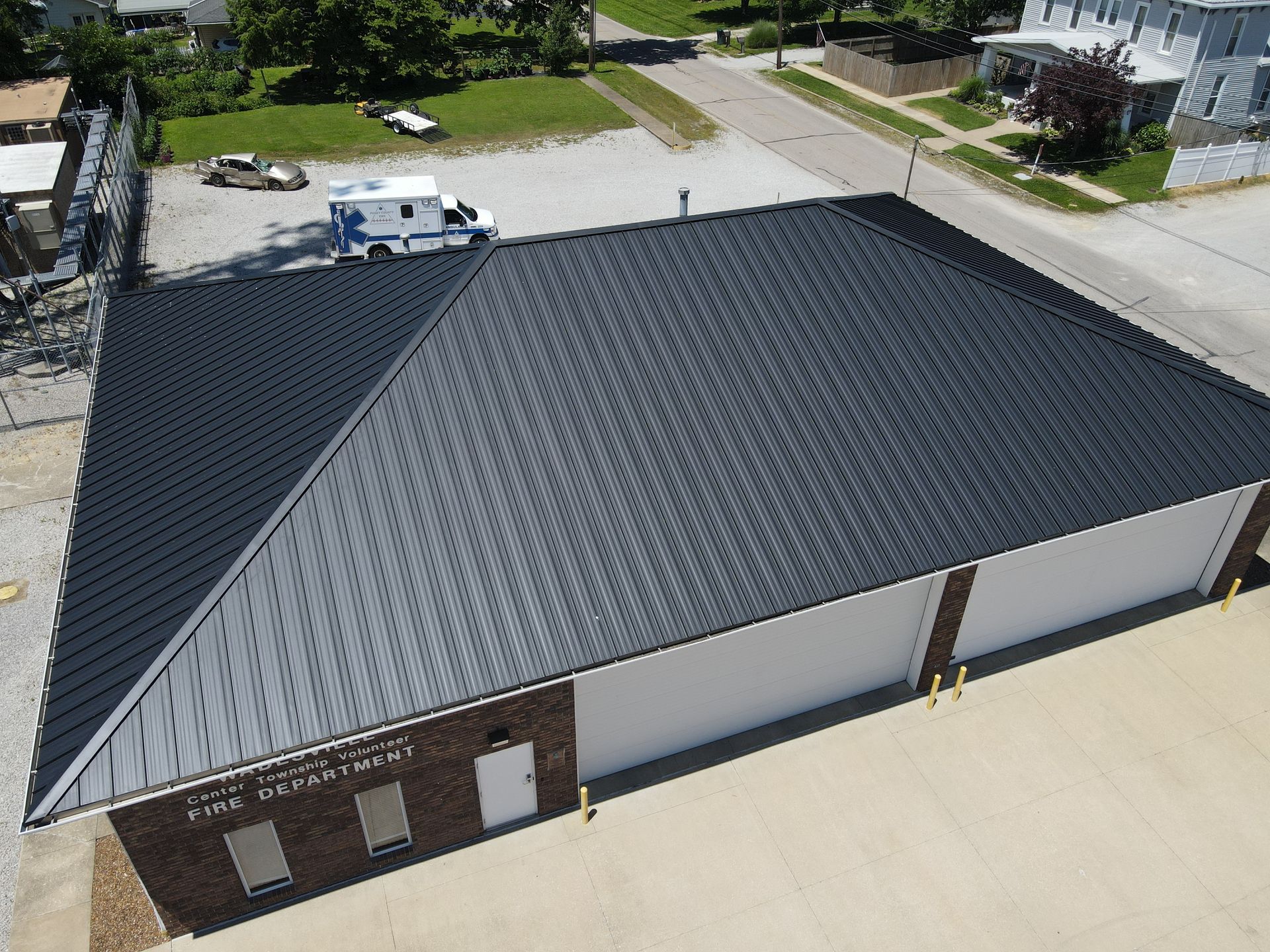 Aerial view of a gray-roofed commercial building beside a street with parked vehicles.