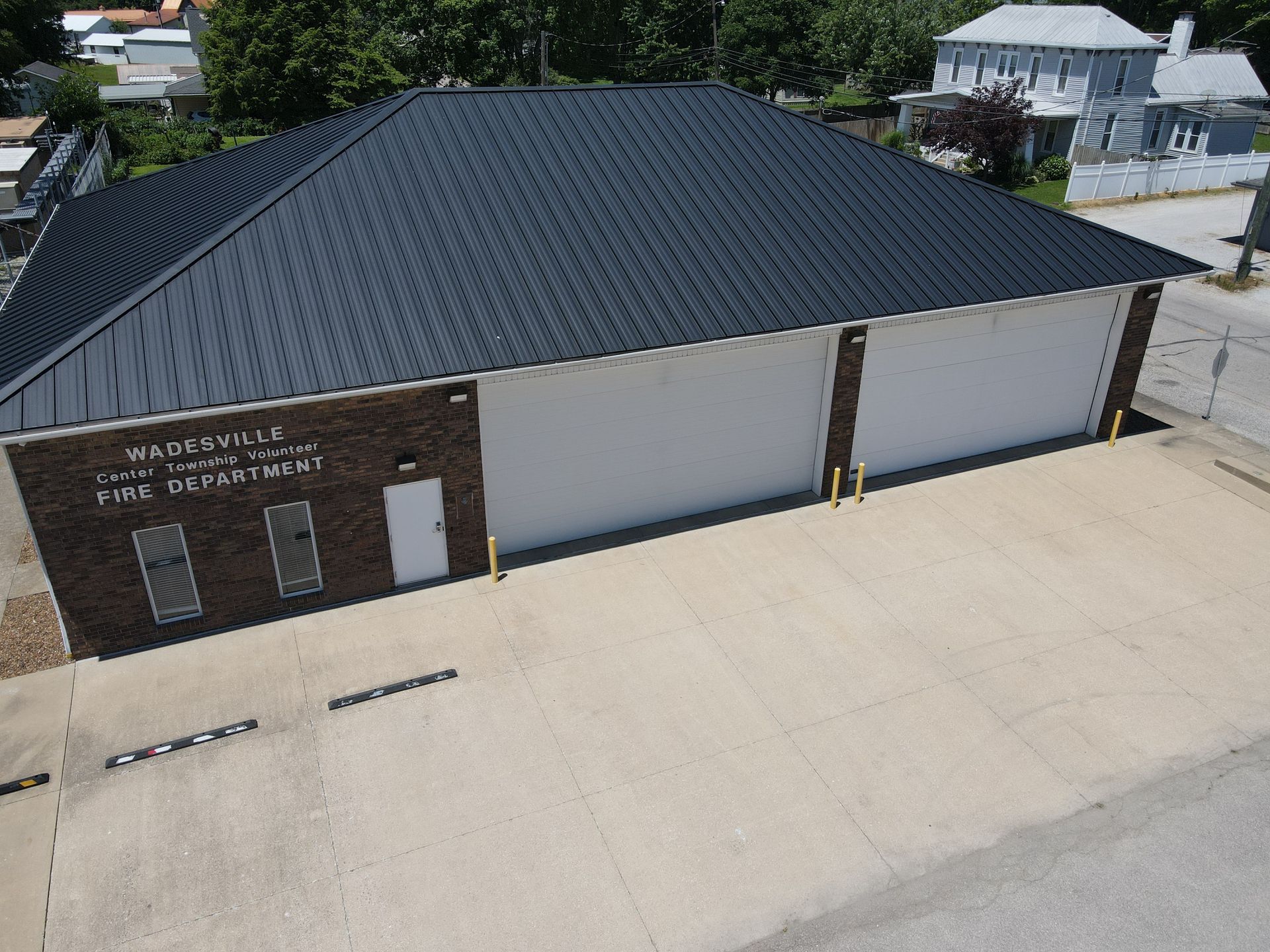 Aerial view of a brick and white industrial building with a dark roof and concrete lot.