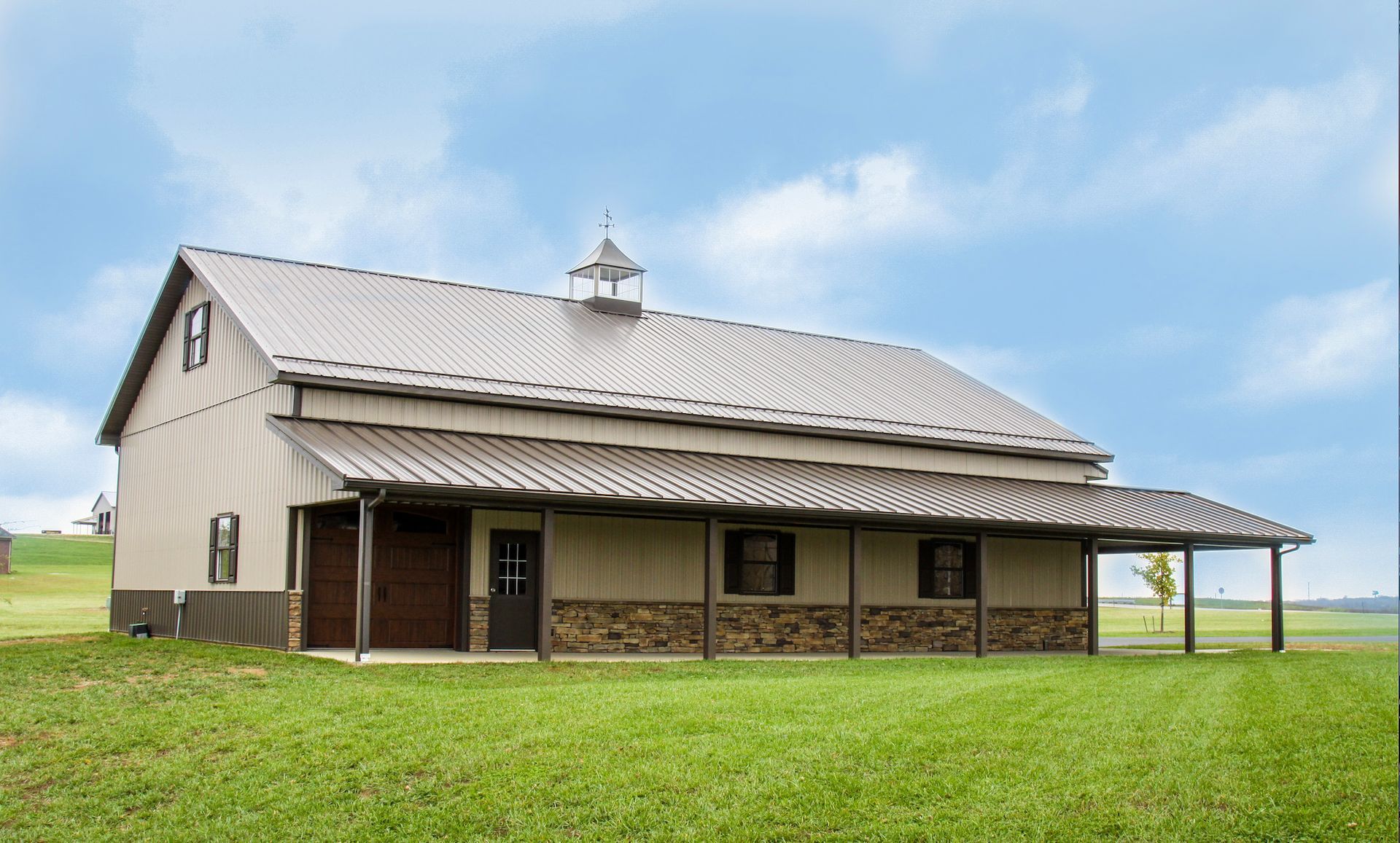 Rustic barn with metal roof and porch on a green field under a blue sky