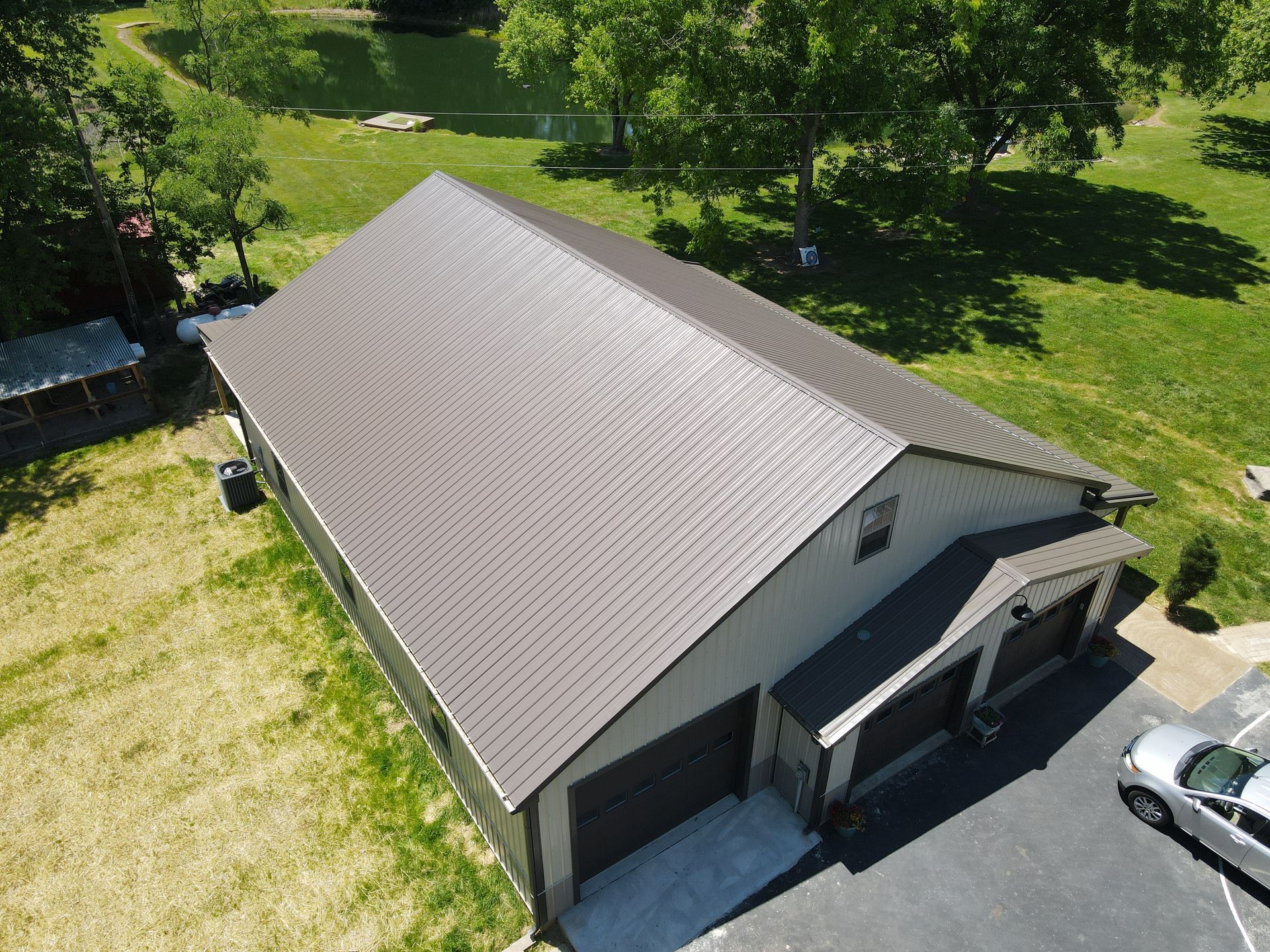Aerial view of a gray-roofed building beside a driveway, surrounded by grass and trees.