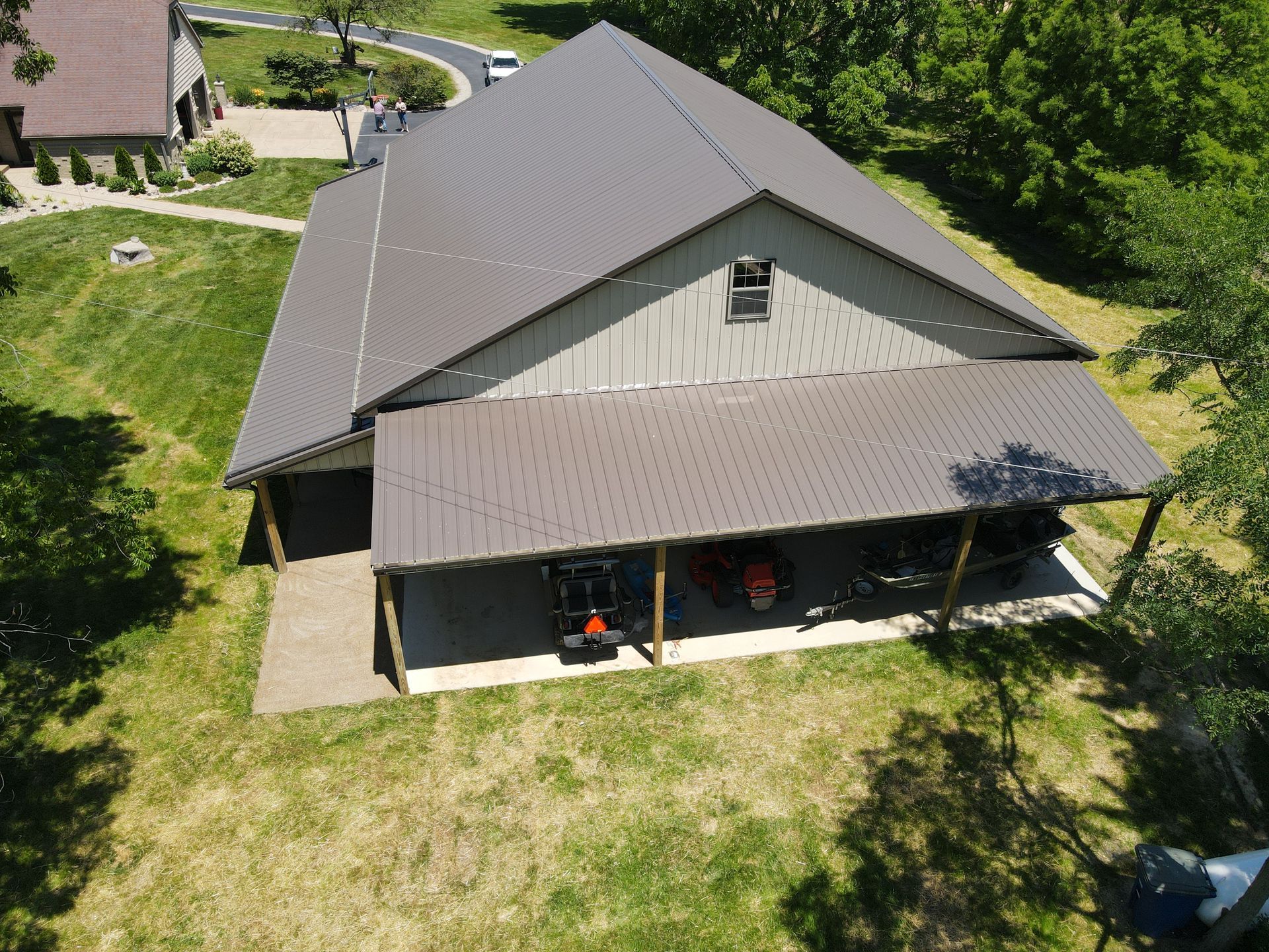 Aerial view of a gray-roofed house with a covered porch, surrounded by grass and trees.