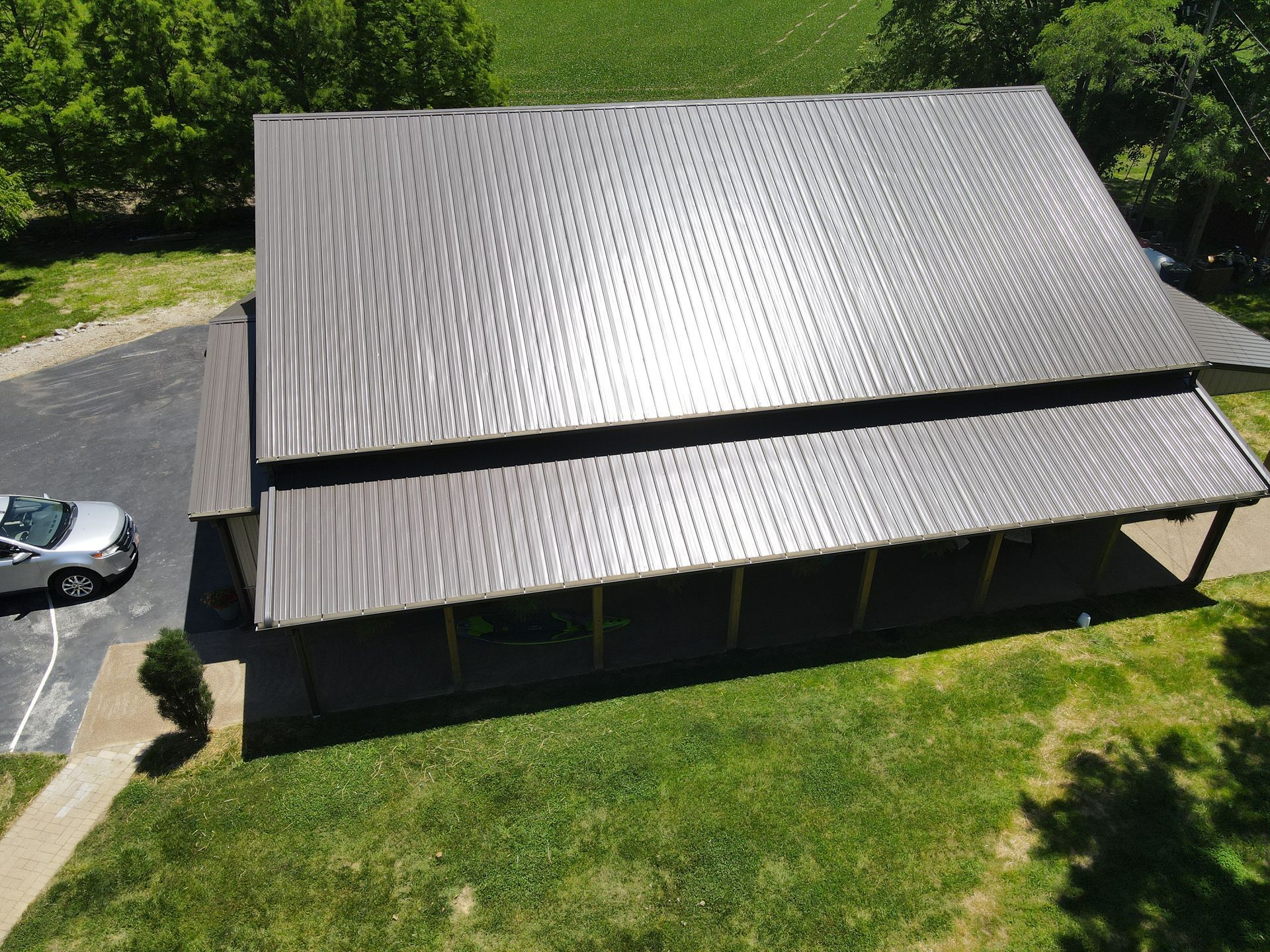 Aerial view of a barn-like building with a dark metal roof, surrounded by grass and a parking lot.