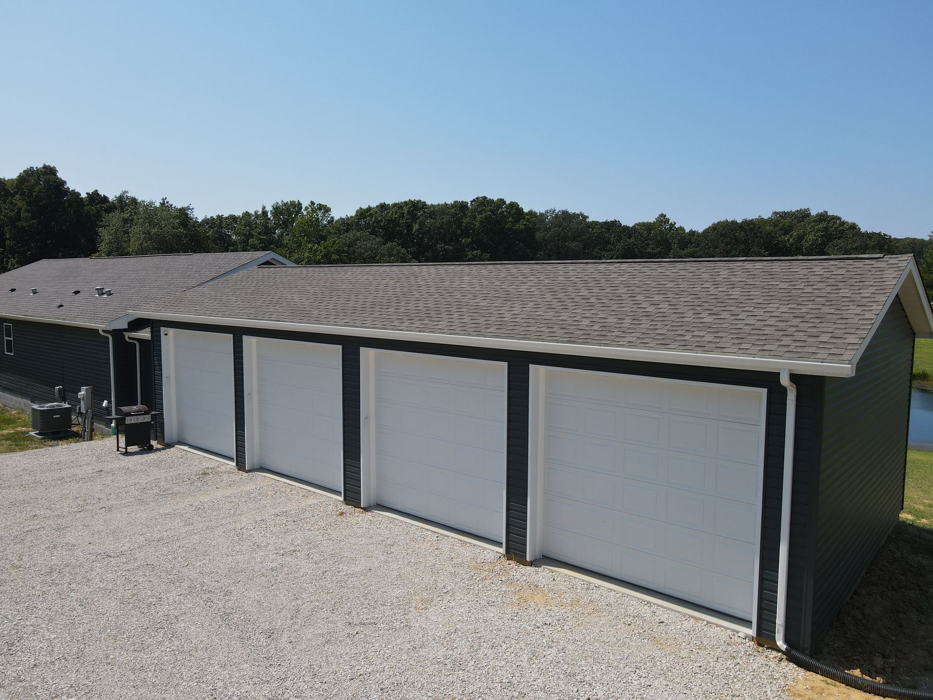 Row of white storage garage doors with dark trim under a shingled roof on a gravel lot