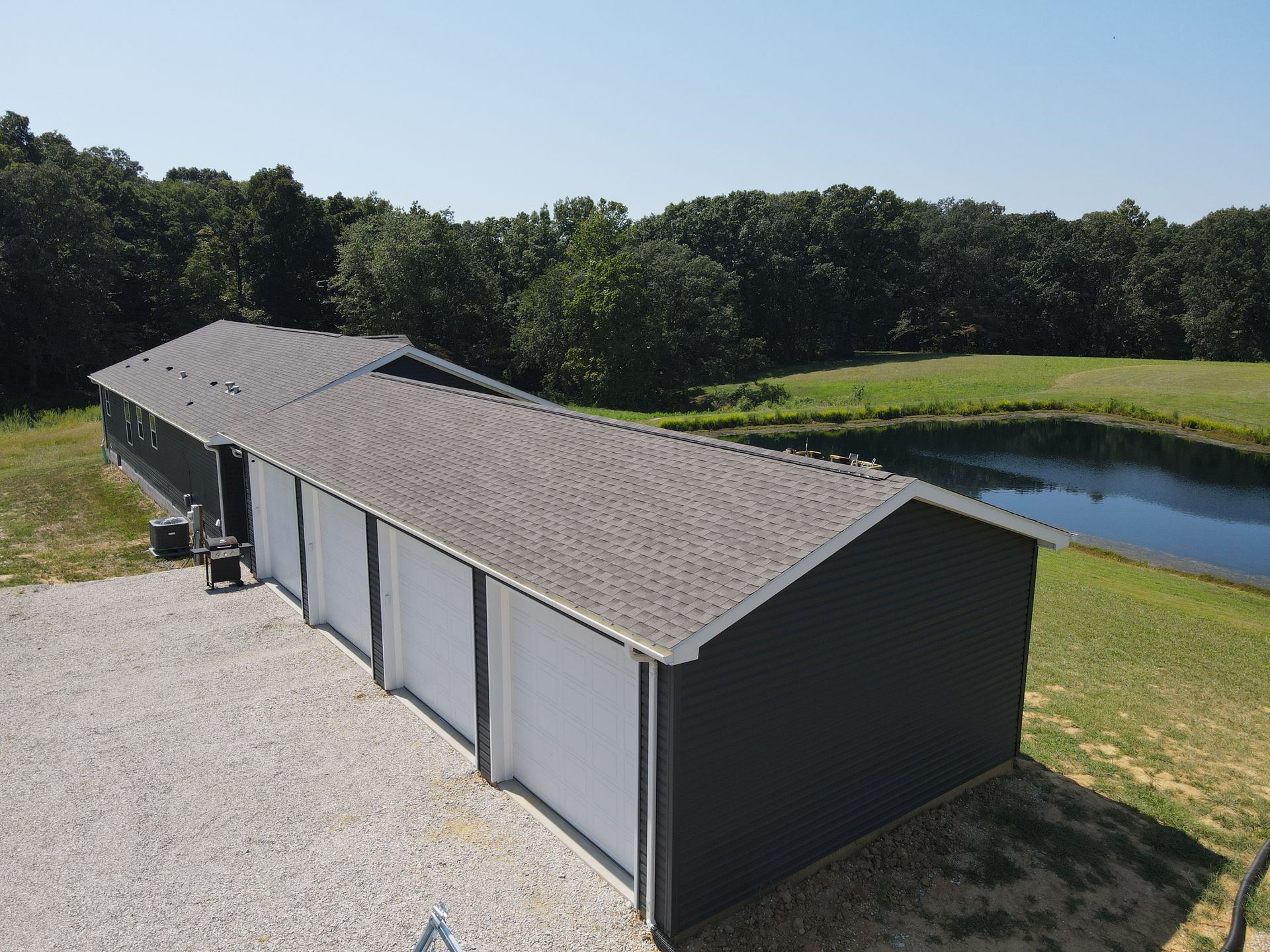Long dark gray storage building beside a pond, with trees and grass in the background