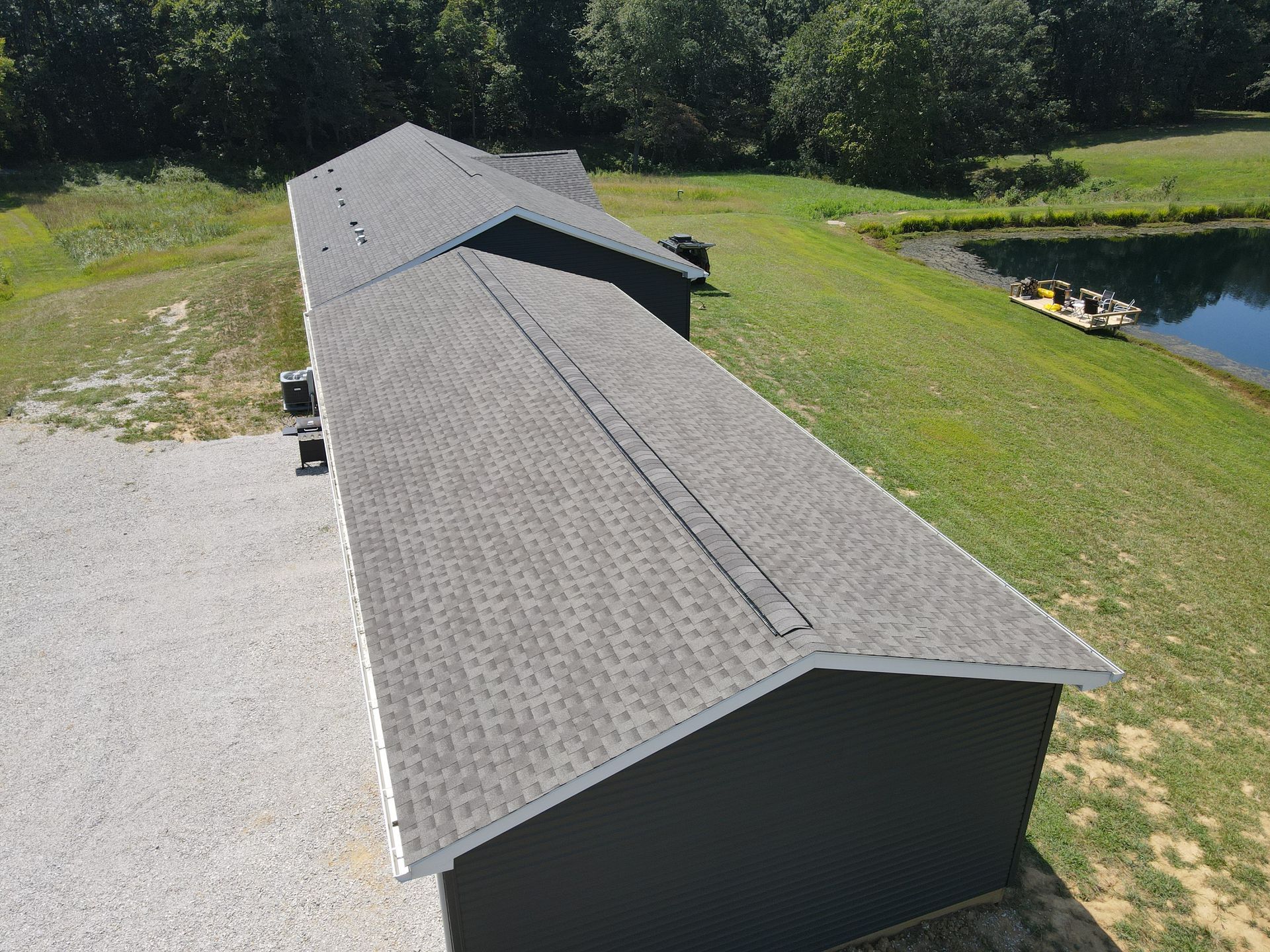 Long gray-roofed building beside a pond, surrounded by grass and trees.