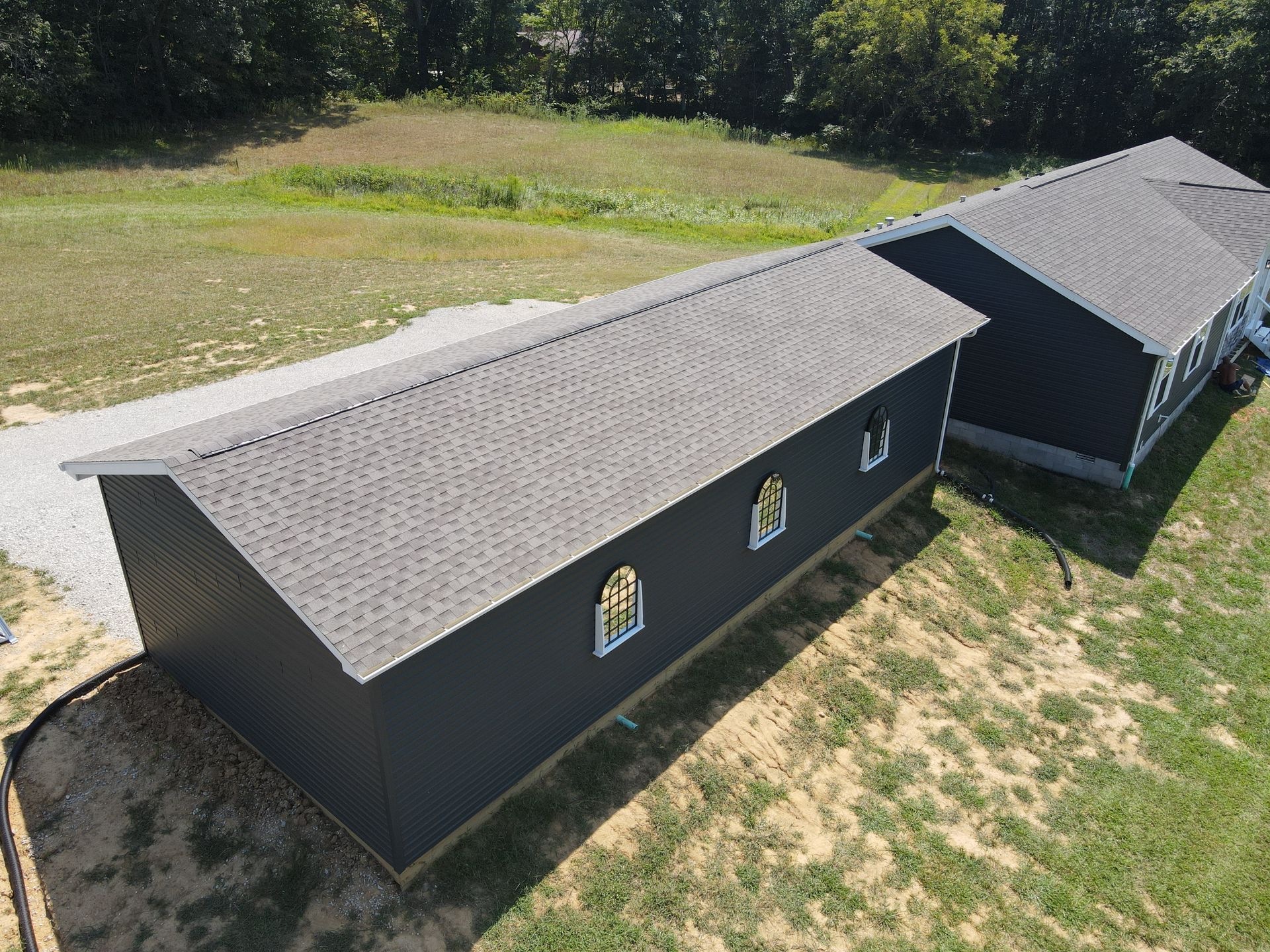 Aerial view of a dark church building with a gray roof beside a grassy field and trees.