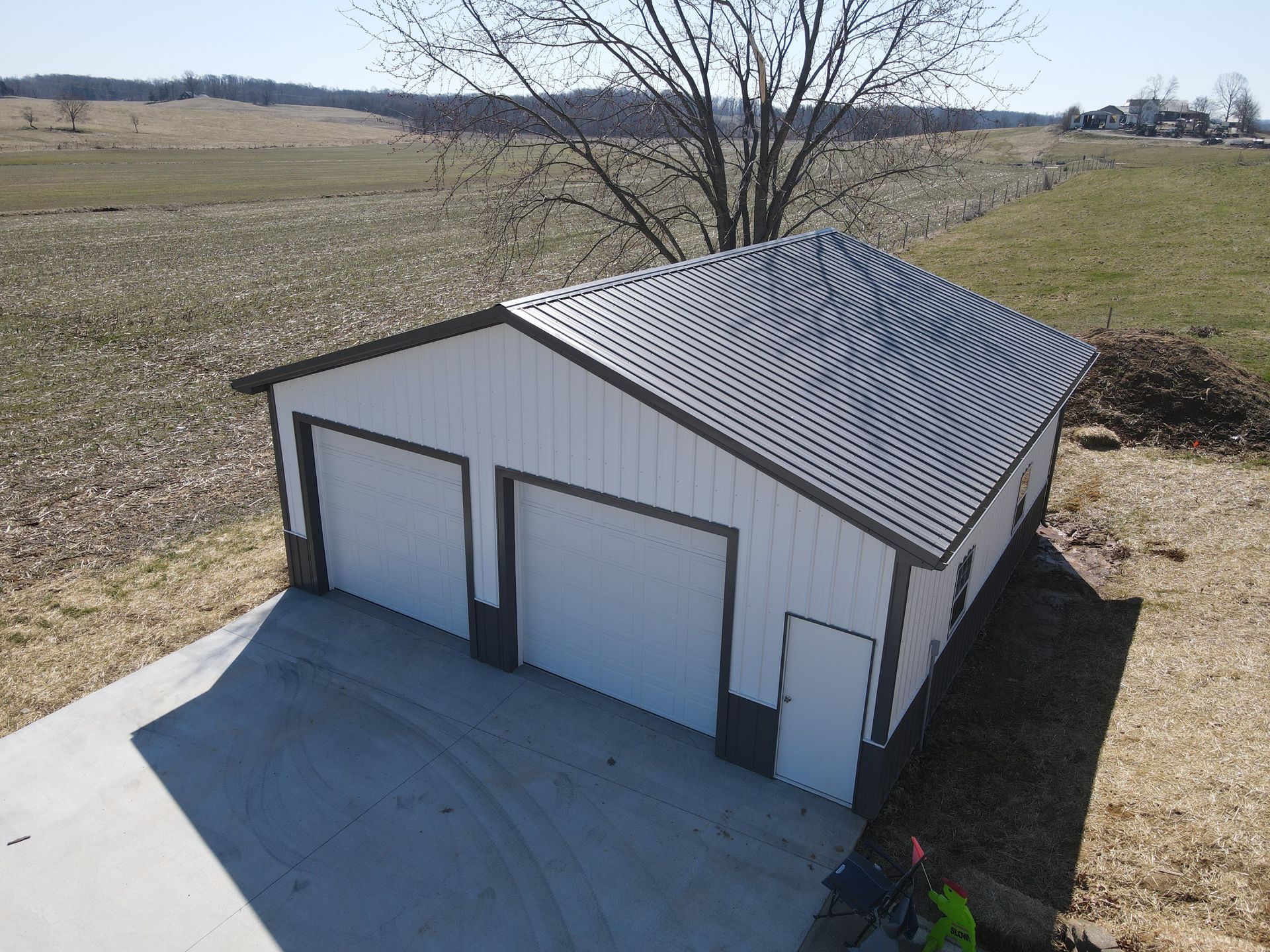 White two-car garage with gray metal roof on a concrete pad in a rural field