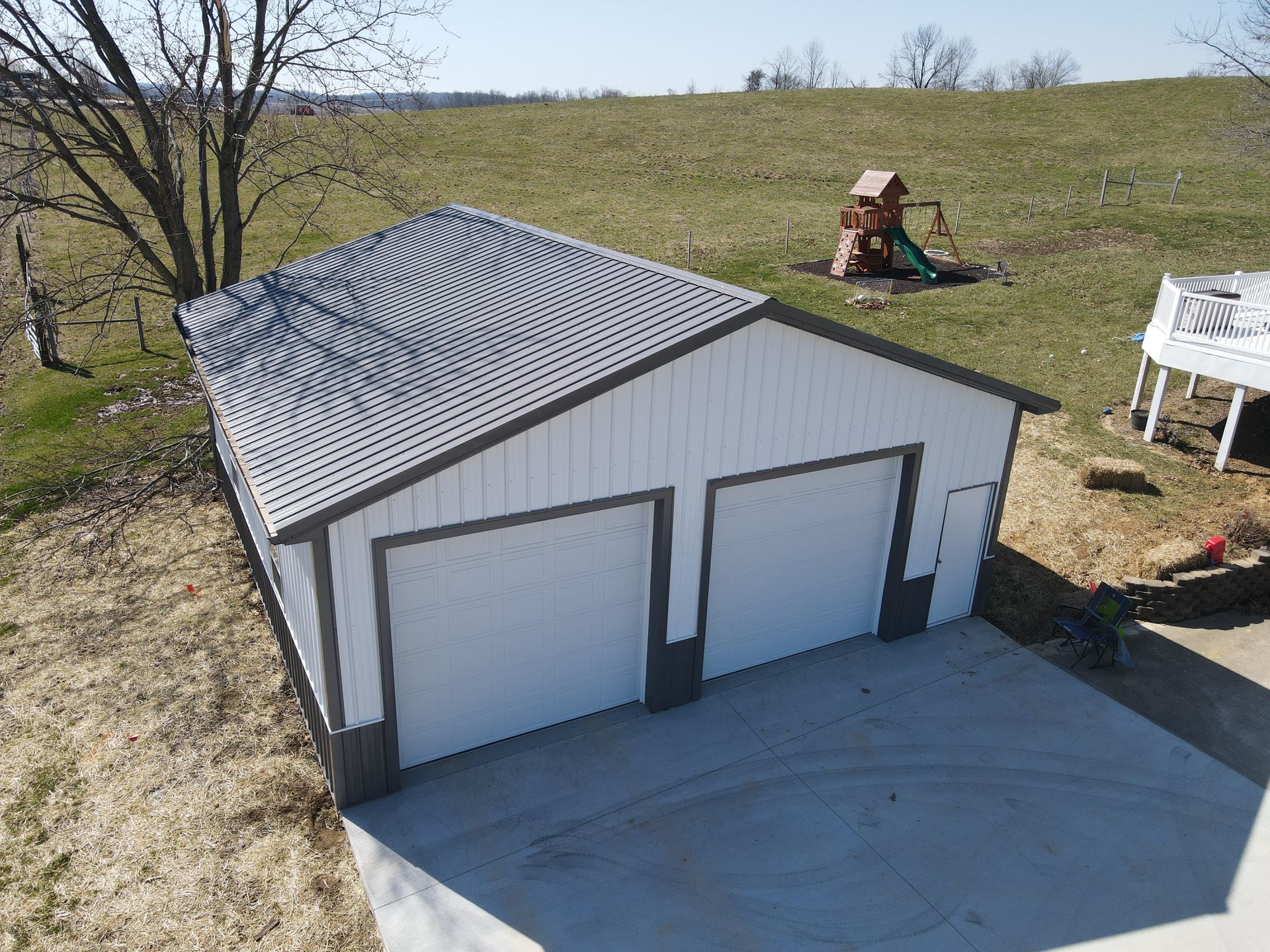 White detached garage with two doors and a concrete driveway on a grassy hill.