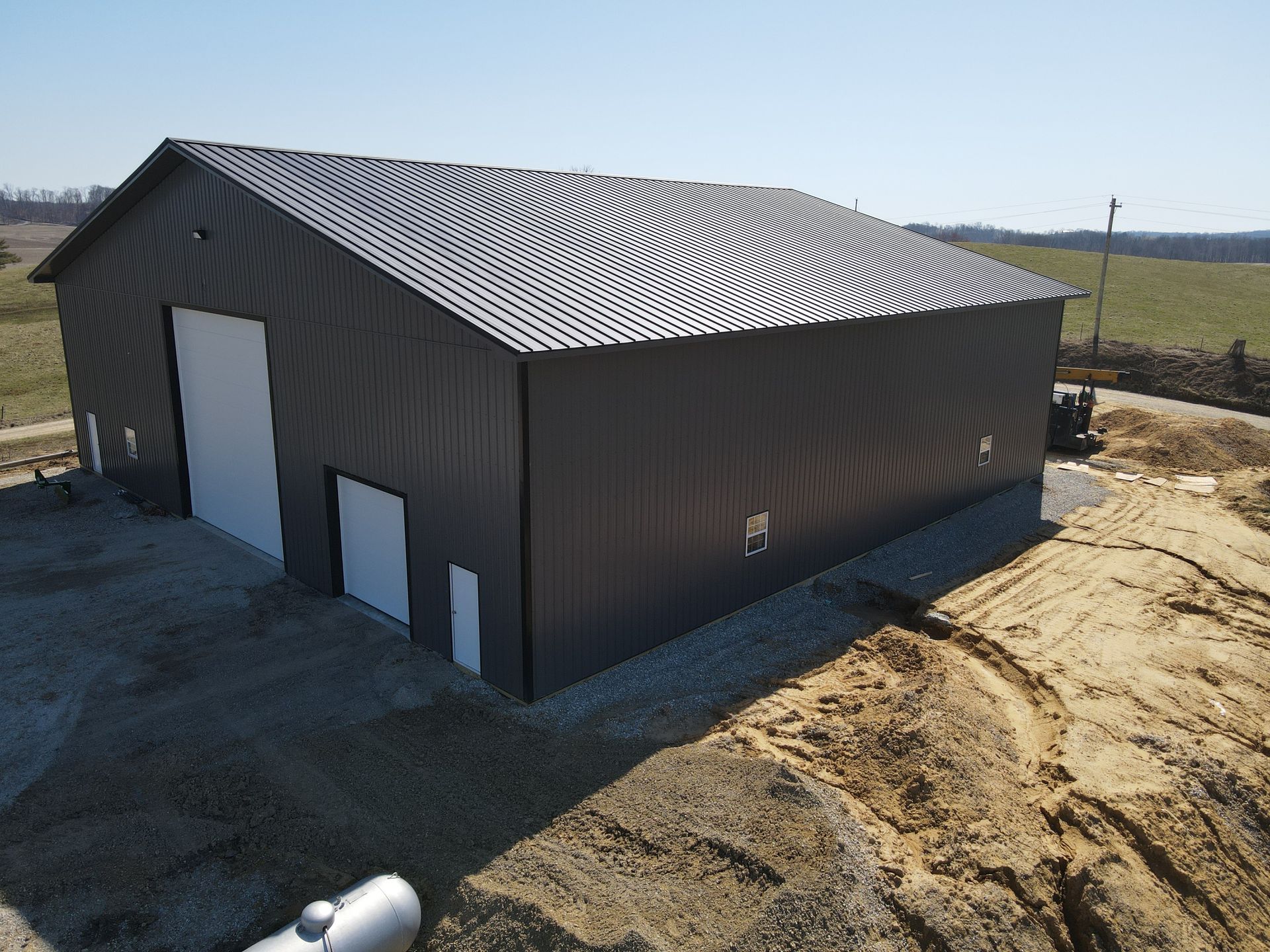 Dark metal barn with white roof on a dirt lot in a rural field
