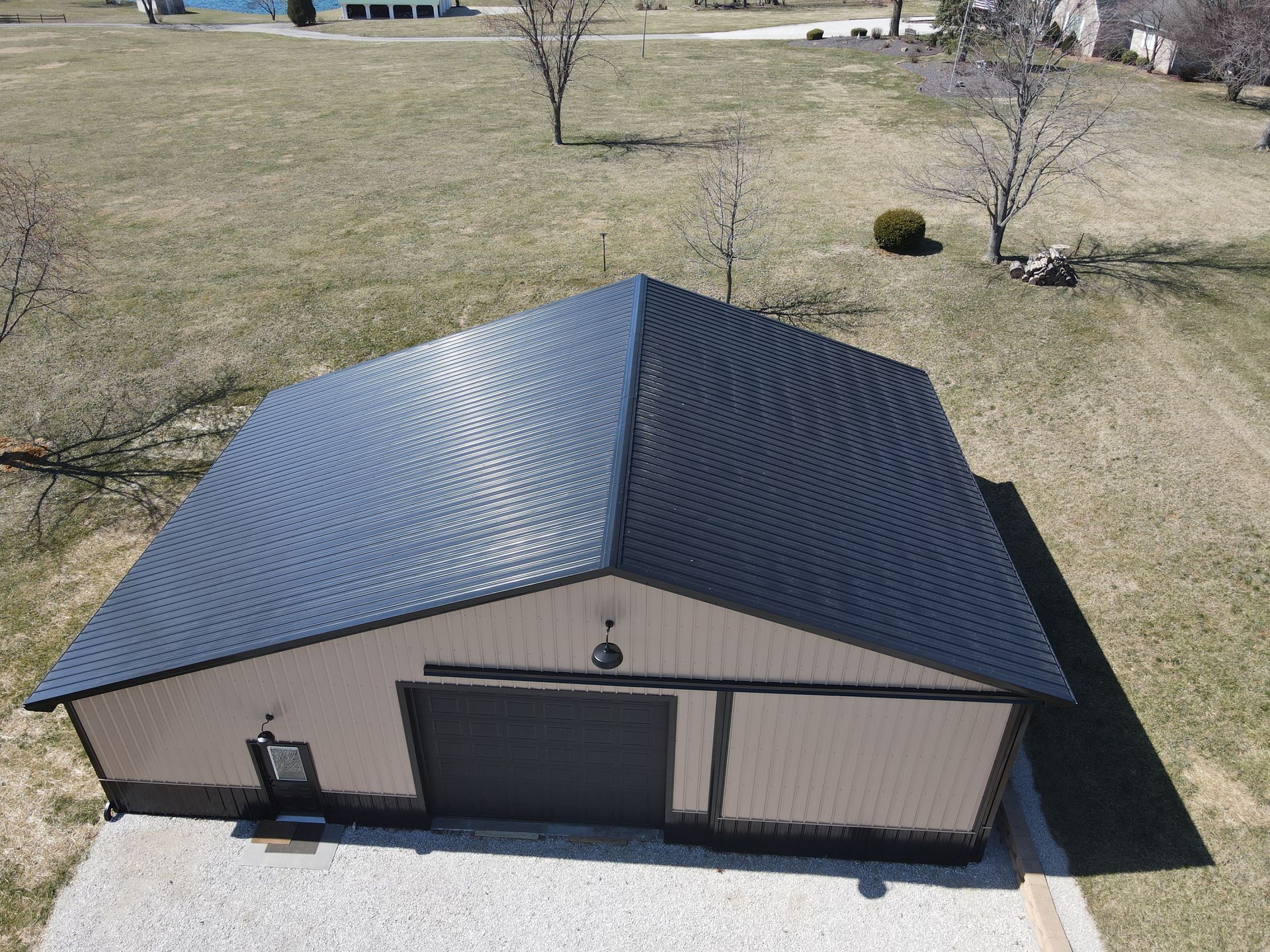Aerial view of a beige garage with a dark metal roof on a grassy lot.