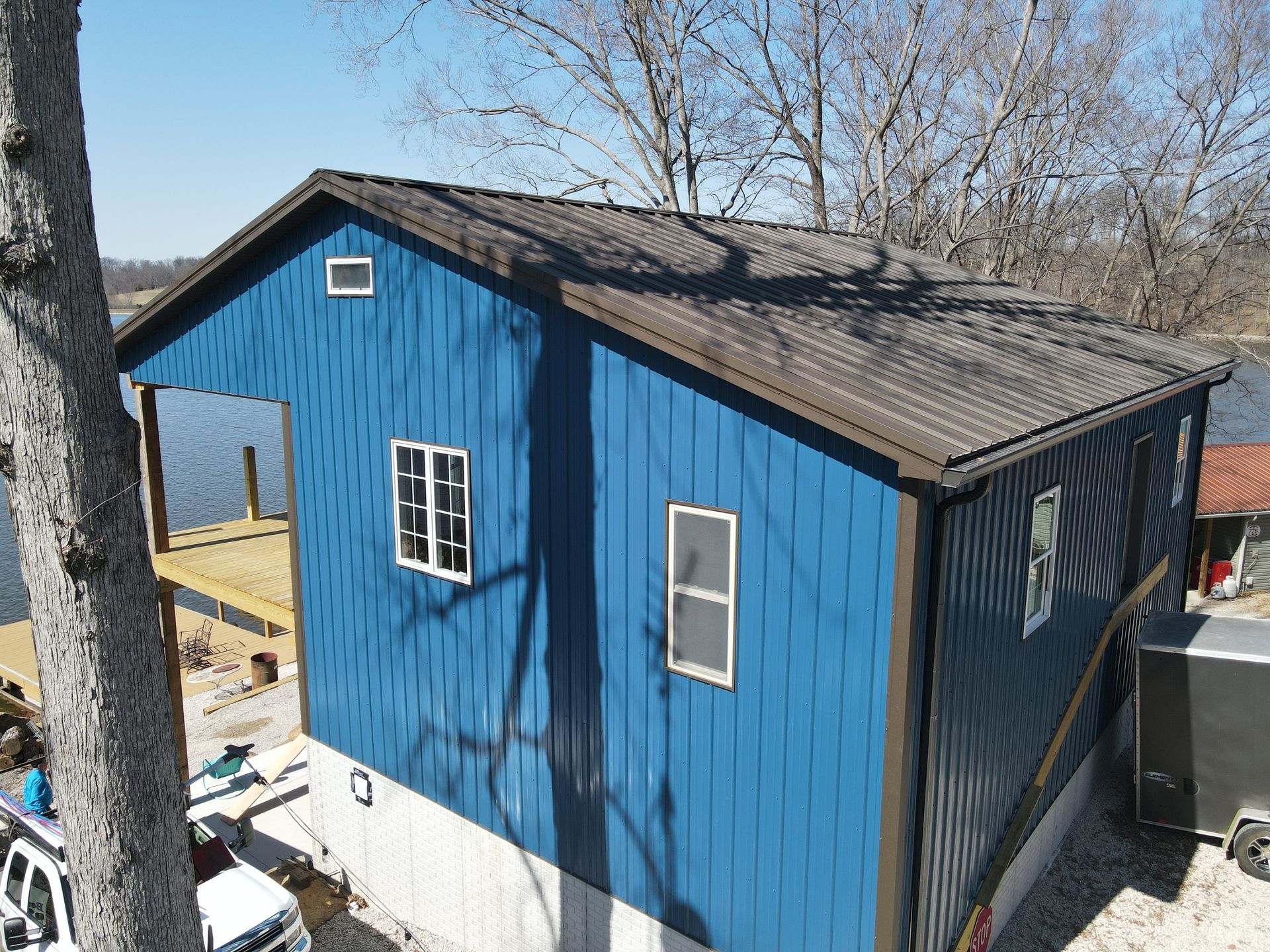 Blue shed-like building with black roof and white-trimmed windows, viewed from above outdoors.