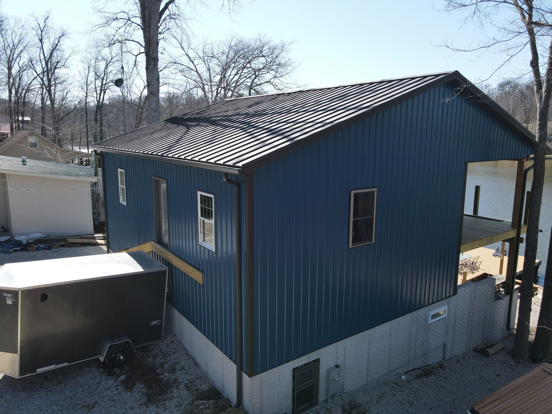Blue-sided house with a sloped roof and white foundation in a wooded yard