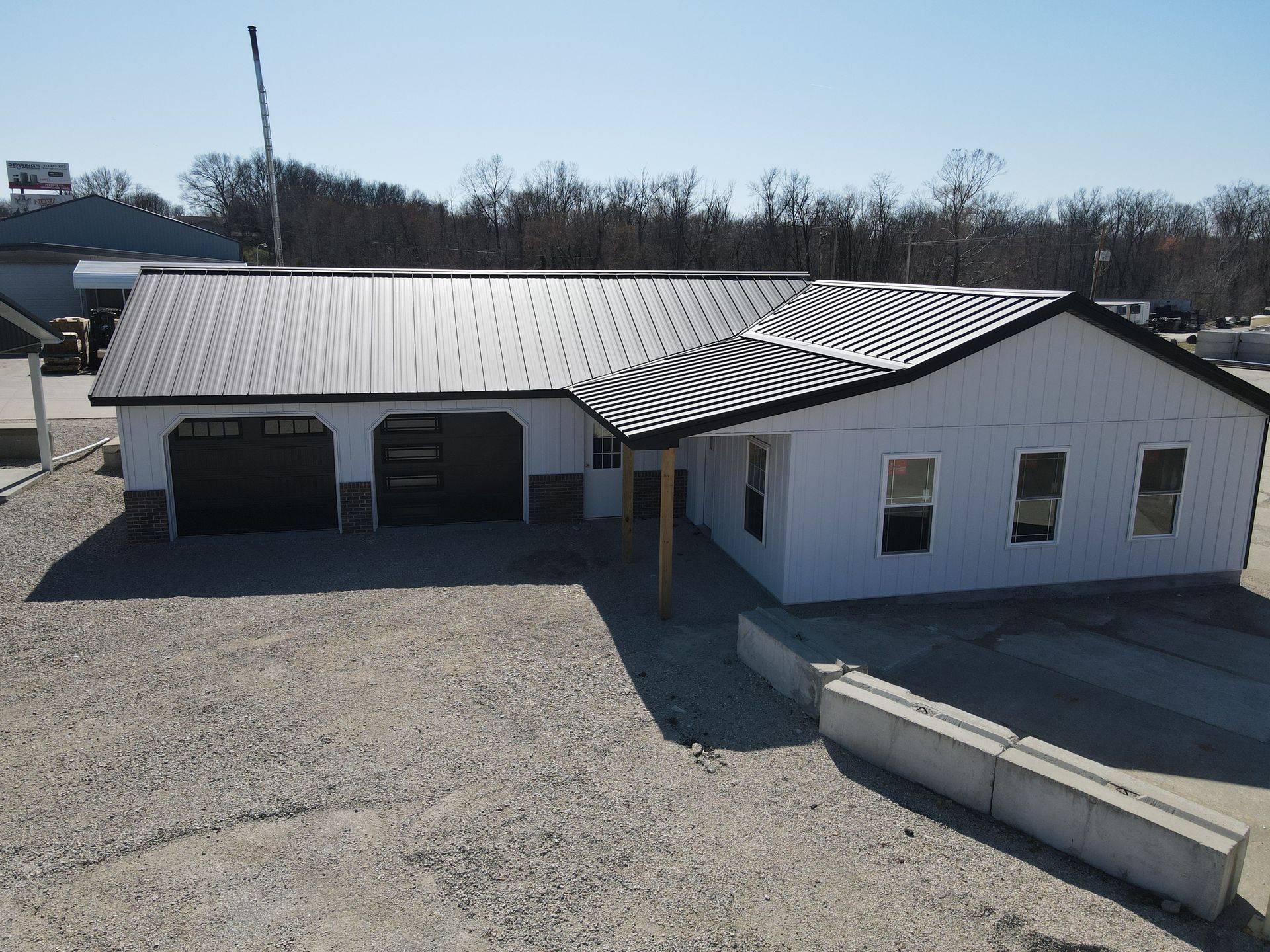Small white building with metal roof, garage doors, and gravel lot under a clear sky