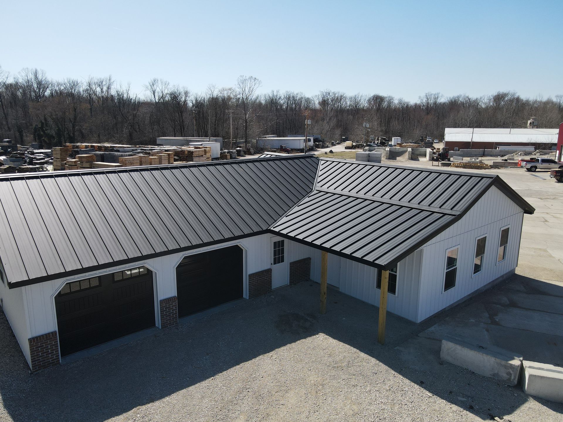 Aerial view of a white industrial building with a dark metal roof and garage doors in a rural lot