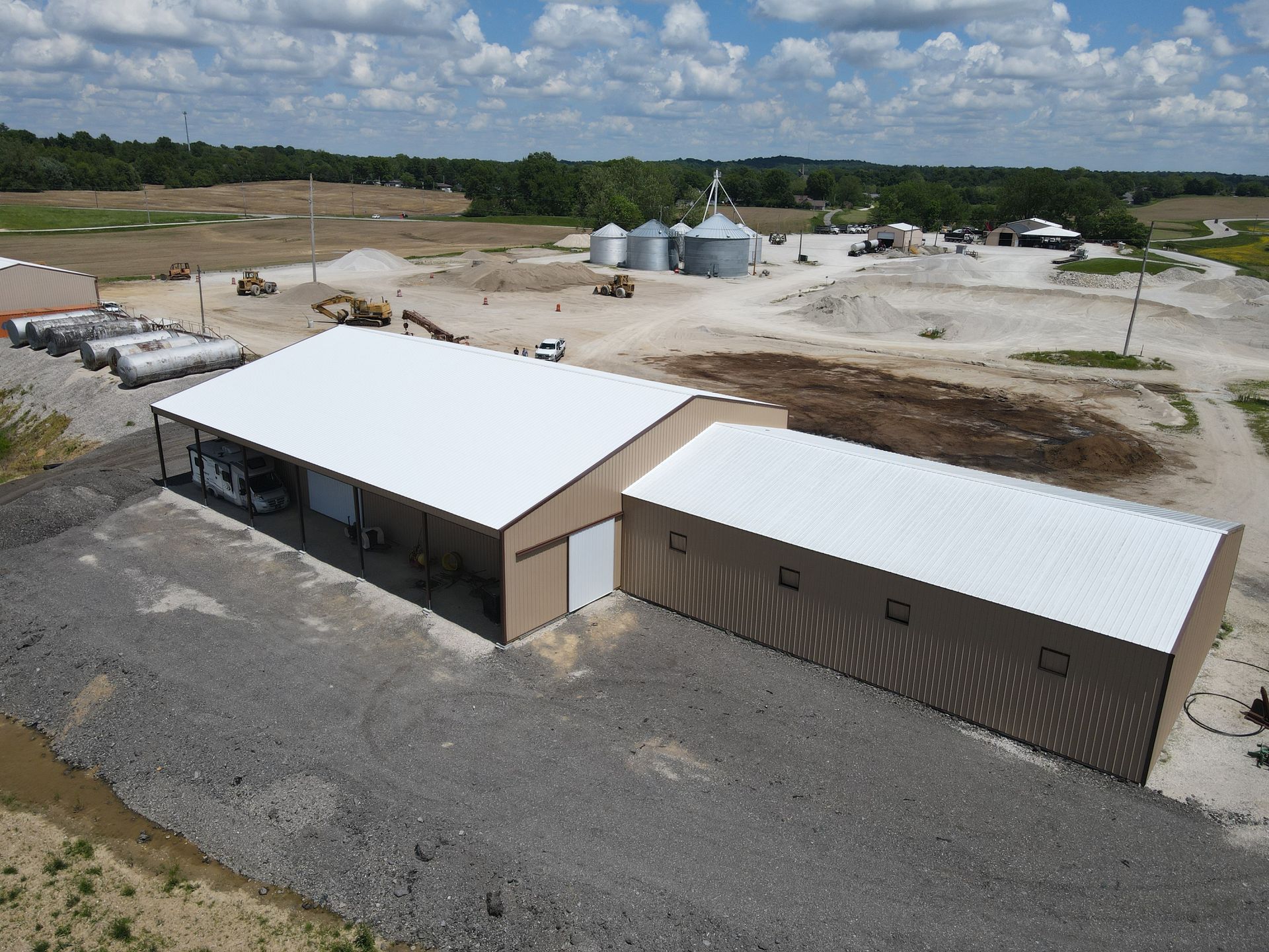 Aerial view of two large tan-and-white industrial buildings in a rural construction site