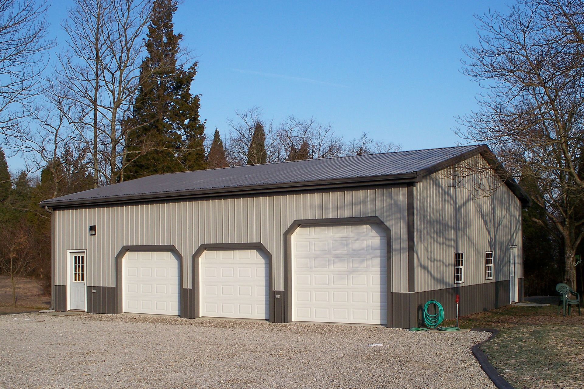 Three-bay beige garage with white doors and a dark roof on a gravel driveway
