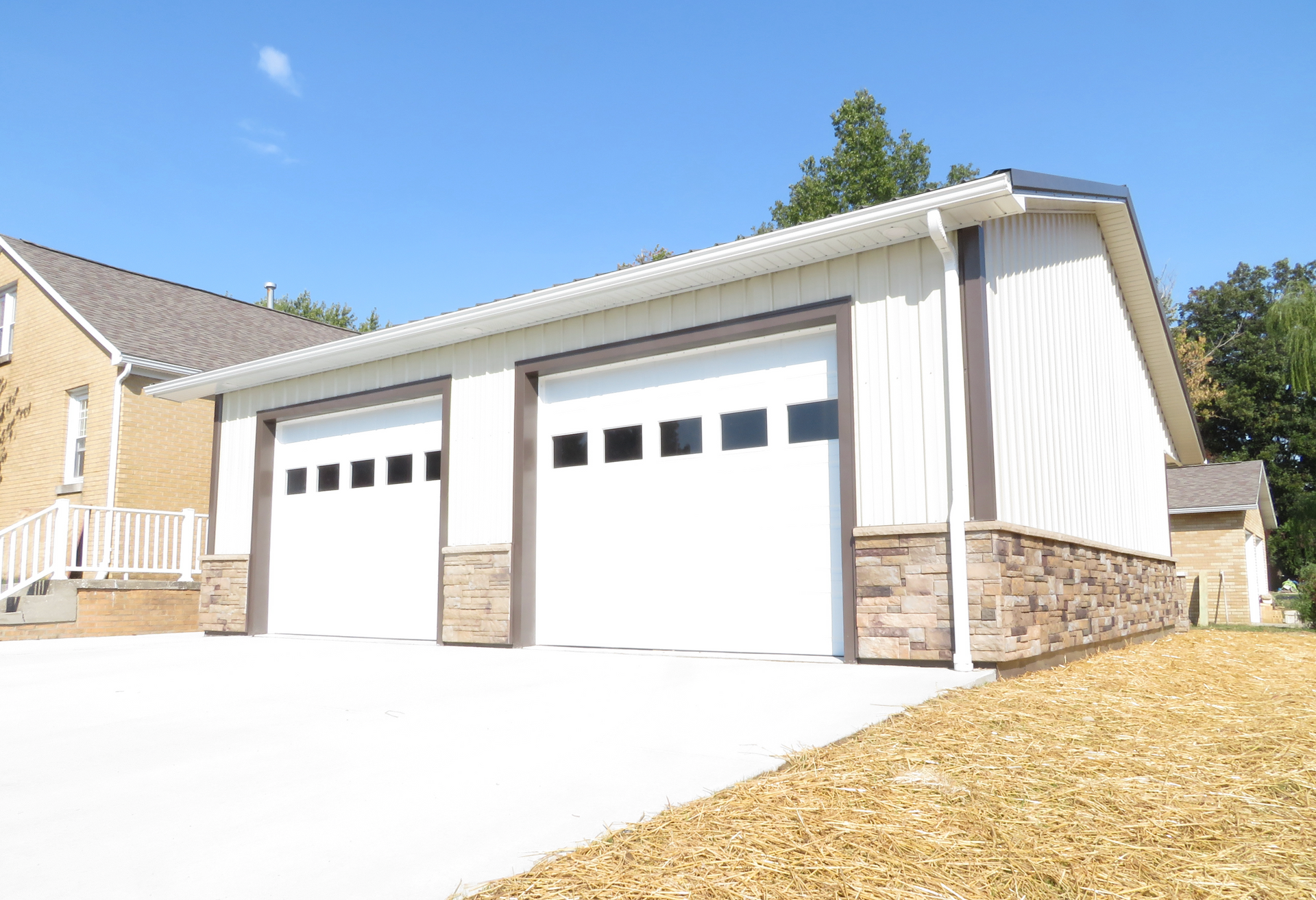 Suburban house with two white garage doors and stone trim on a sunny day