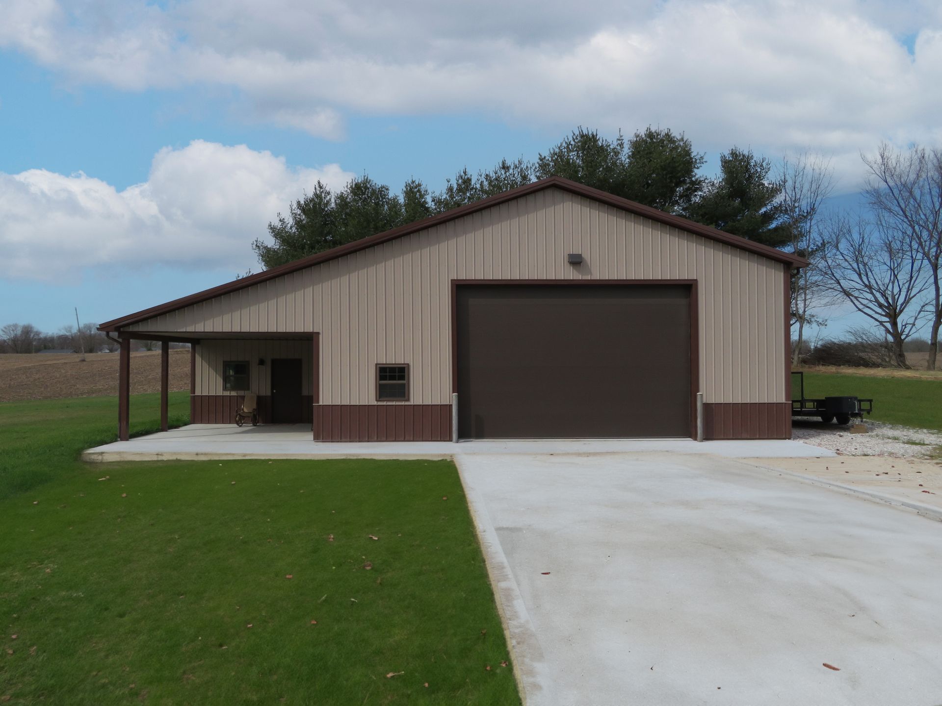 Large tan metal garage with a concrete driveway and green lawn under a cloudy sky.
