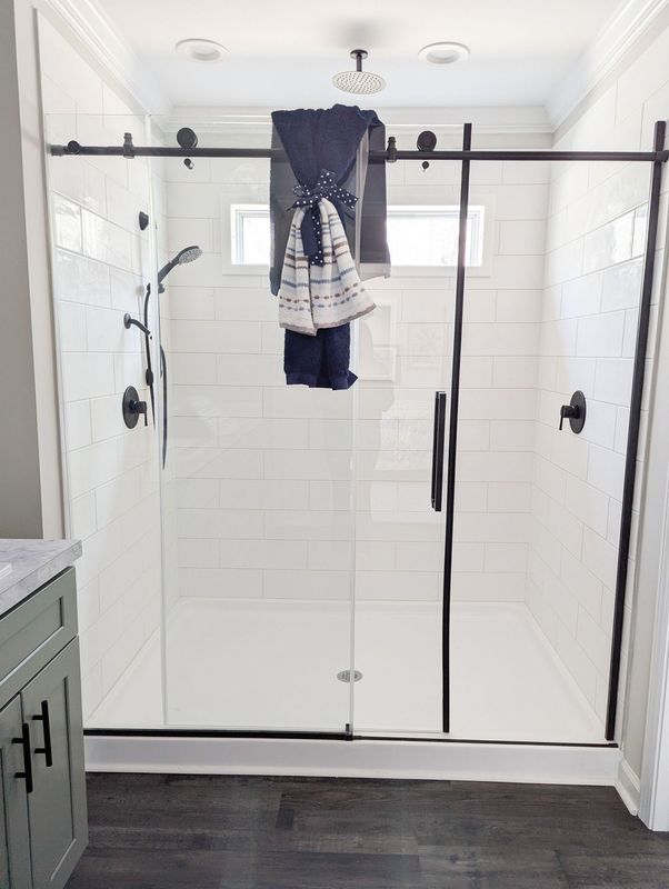A glass walk-in shower with matte black hardware and white subway tile, featuring a towel draped over the door track.