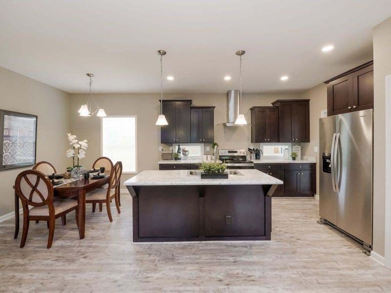 A modern kitchen with dark brown cabinets, a large white-topped island, stainless steel appliances, and a dining area.