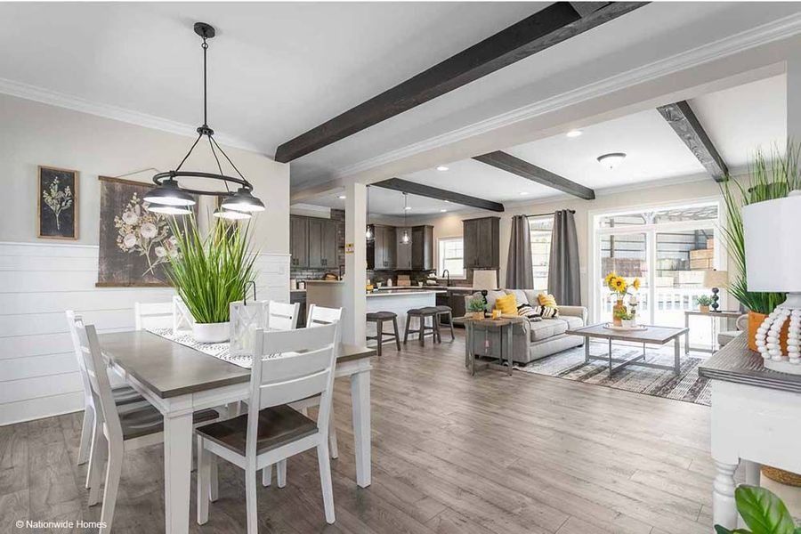 An open-concept living area with a white dining set, modern farmhouse decor, and wooden ceiling beams.