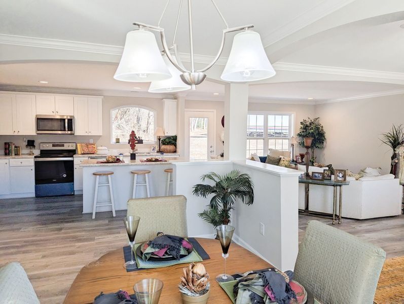 A sunlit open-concept home interior featuring a kitchen with white cabinets, a dining area, and a cozy living room space.