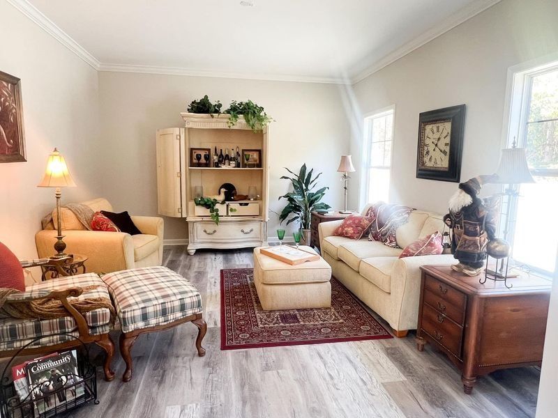 Living room with a sofa, armchair, ottoman, and large armoire on a red patterned rug over light wood-look flooring.
