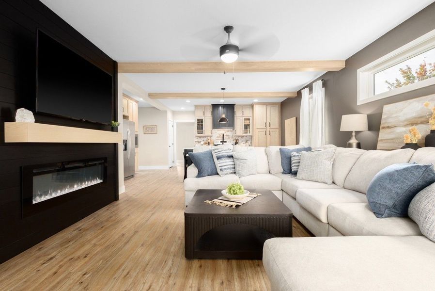 A modern living room with a large white sectional, a black fireplace wall, light wood floors, and an open kitchen background.