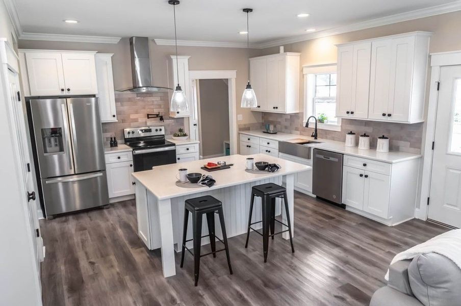 A bright, modern kitchen featuring white cabinets, stainless steel appliances, a center island with two black stools.