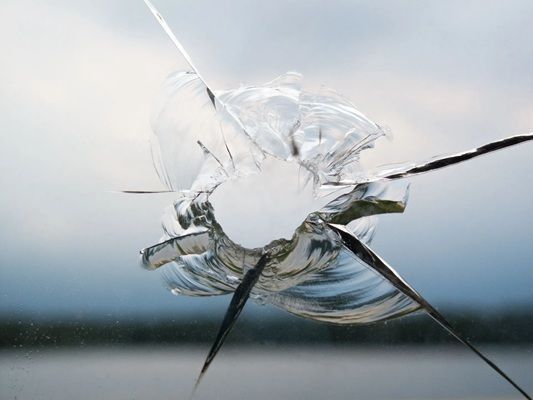 Broken glass with cracks radiating across a white and blue sky reflection