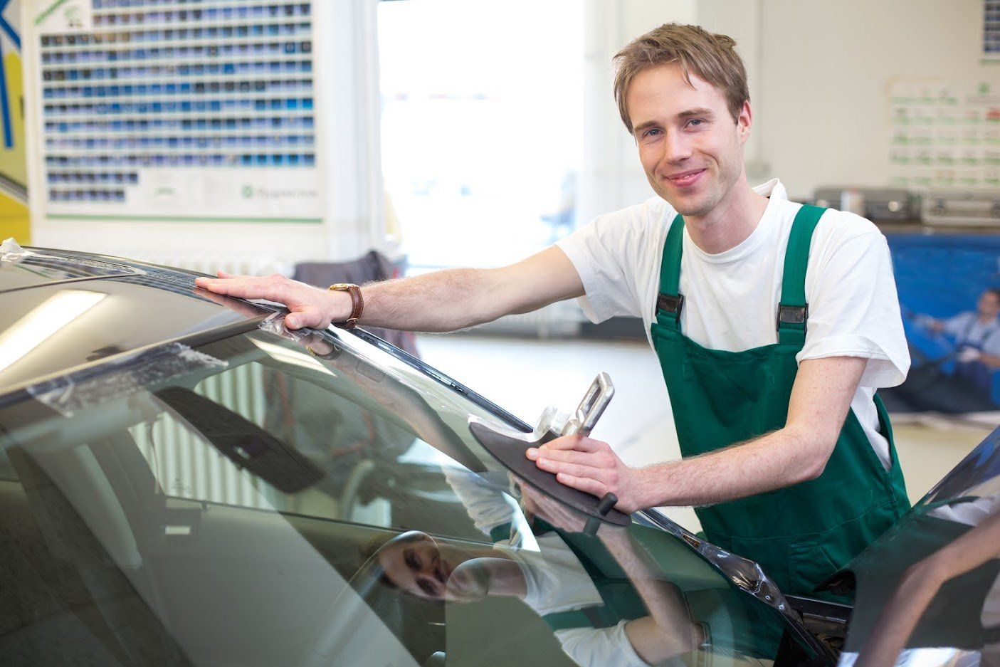 Mechanic in green overalls washing a car windshield in a bright auto shop