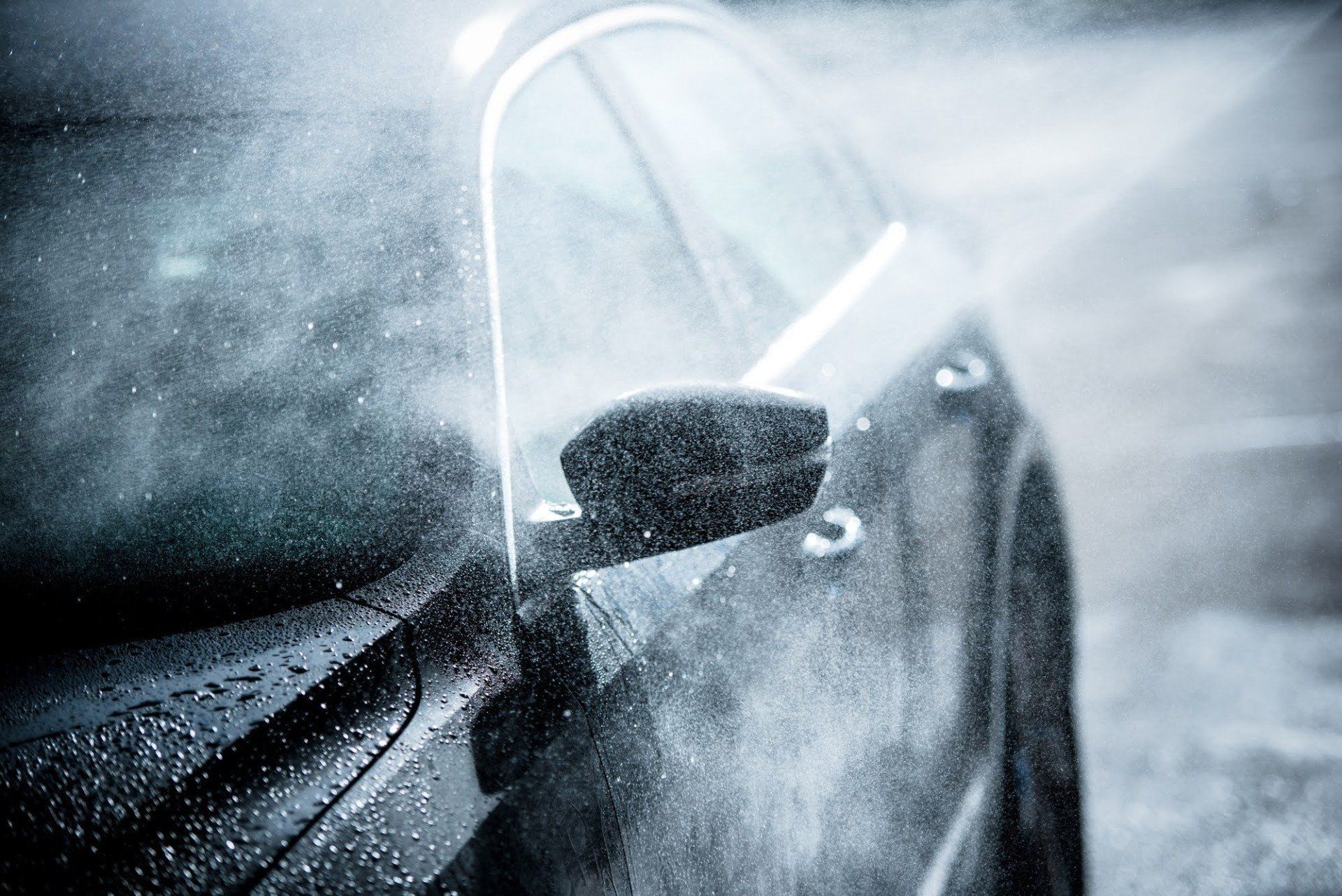 Rain-soaked black car side mirror and door, with water spraying across the window