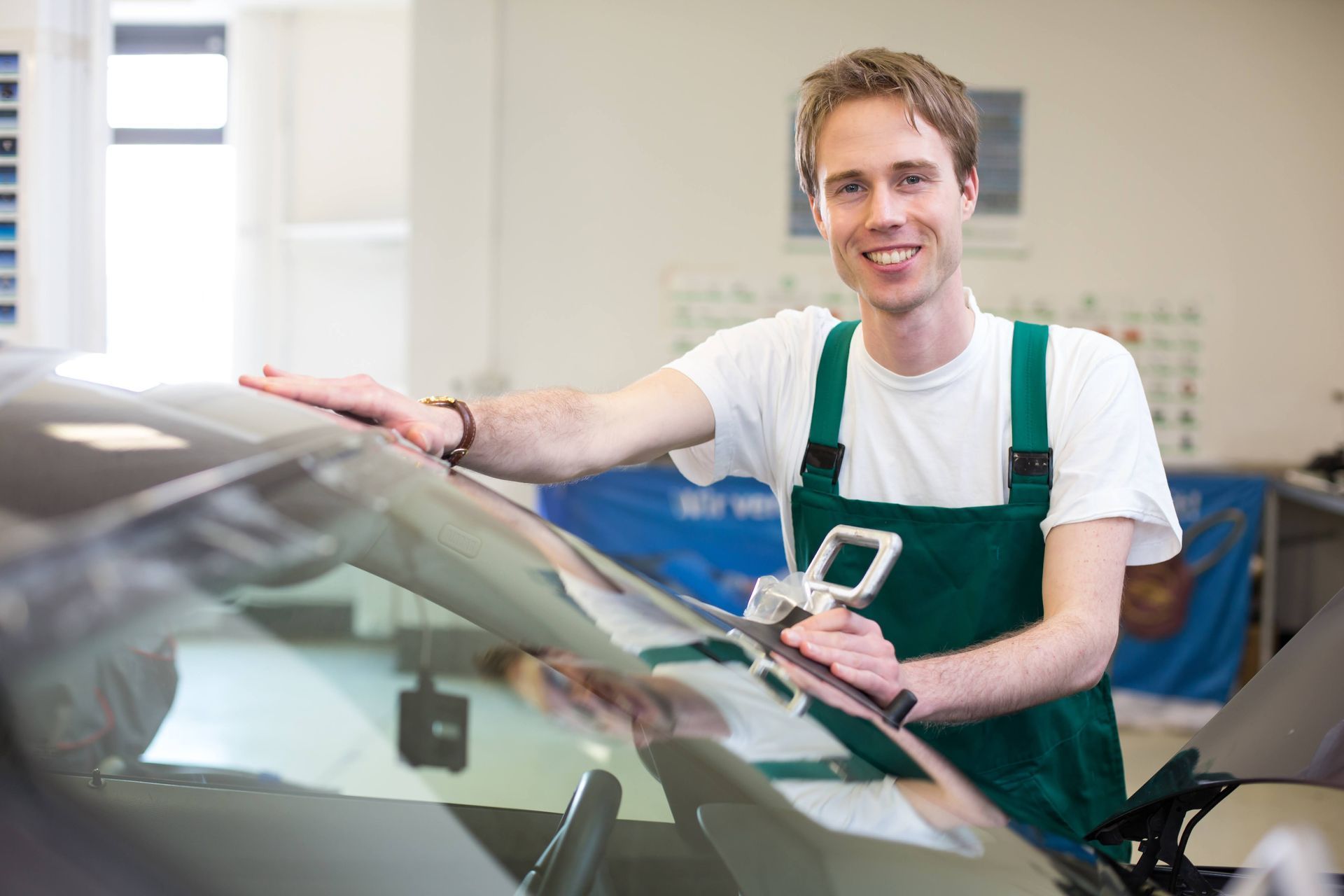 Mechanic smiling and polishing a car windshield in an auto shop