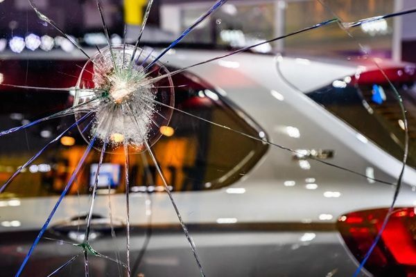 Shattered car window with a large impact crack, reflecting lights on a silver vehicle