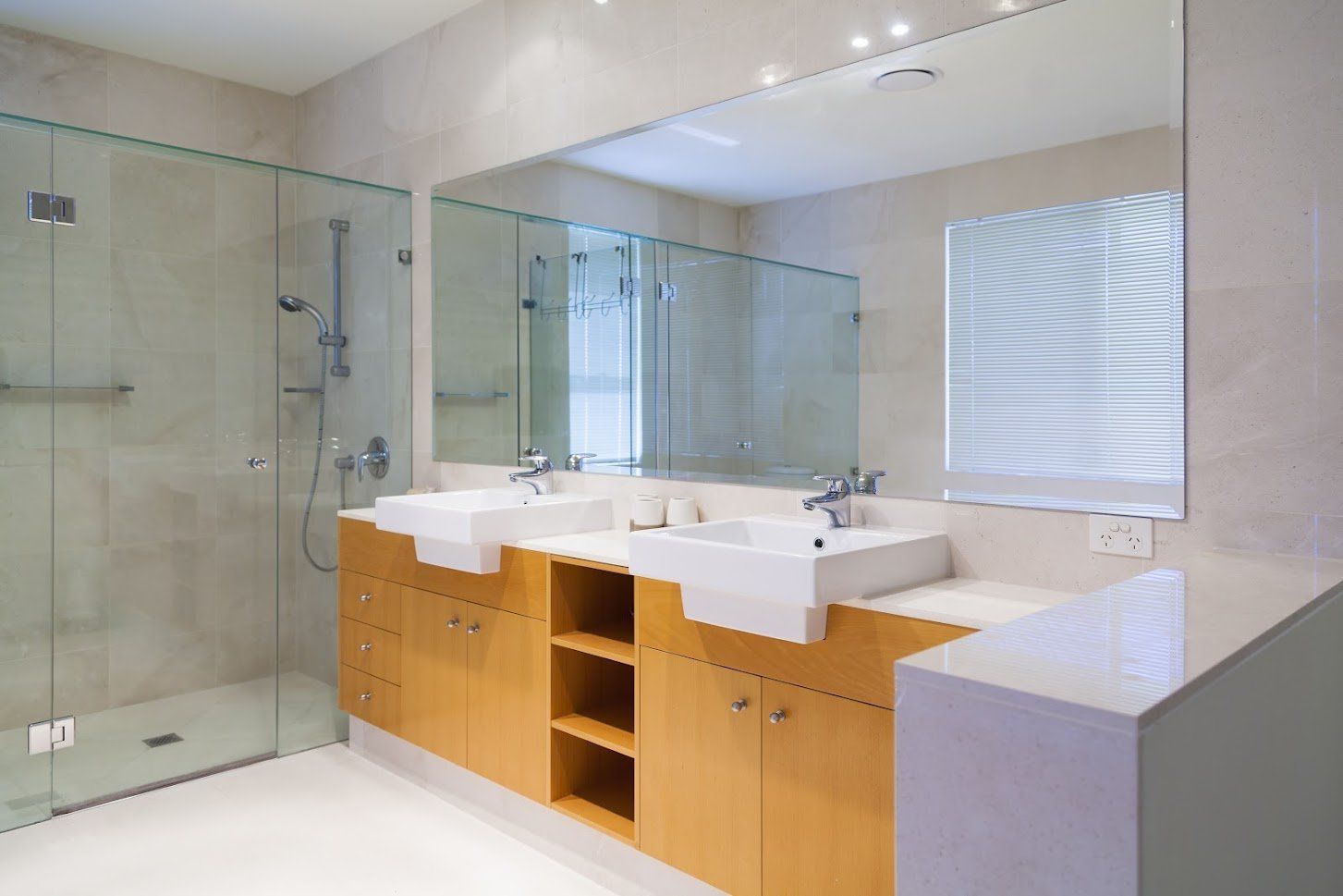 Modern bathroom with double sinks, wooden vanity, large mirror, and glass shower enclosure