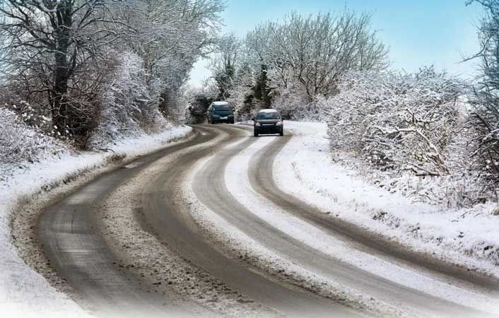 Snow-covered winding road with two cars driving through a frosty winter landscape