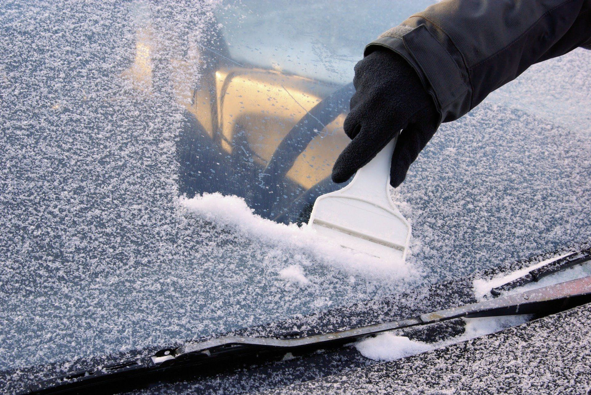 Person scraping ice off a car windshield with a brush in winter.