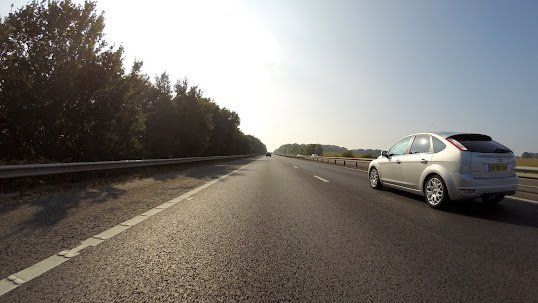Silver car on a highway shoulder beside a guardrail, with trees lining the road ahead.