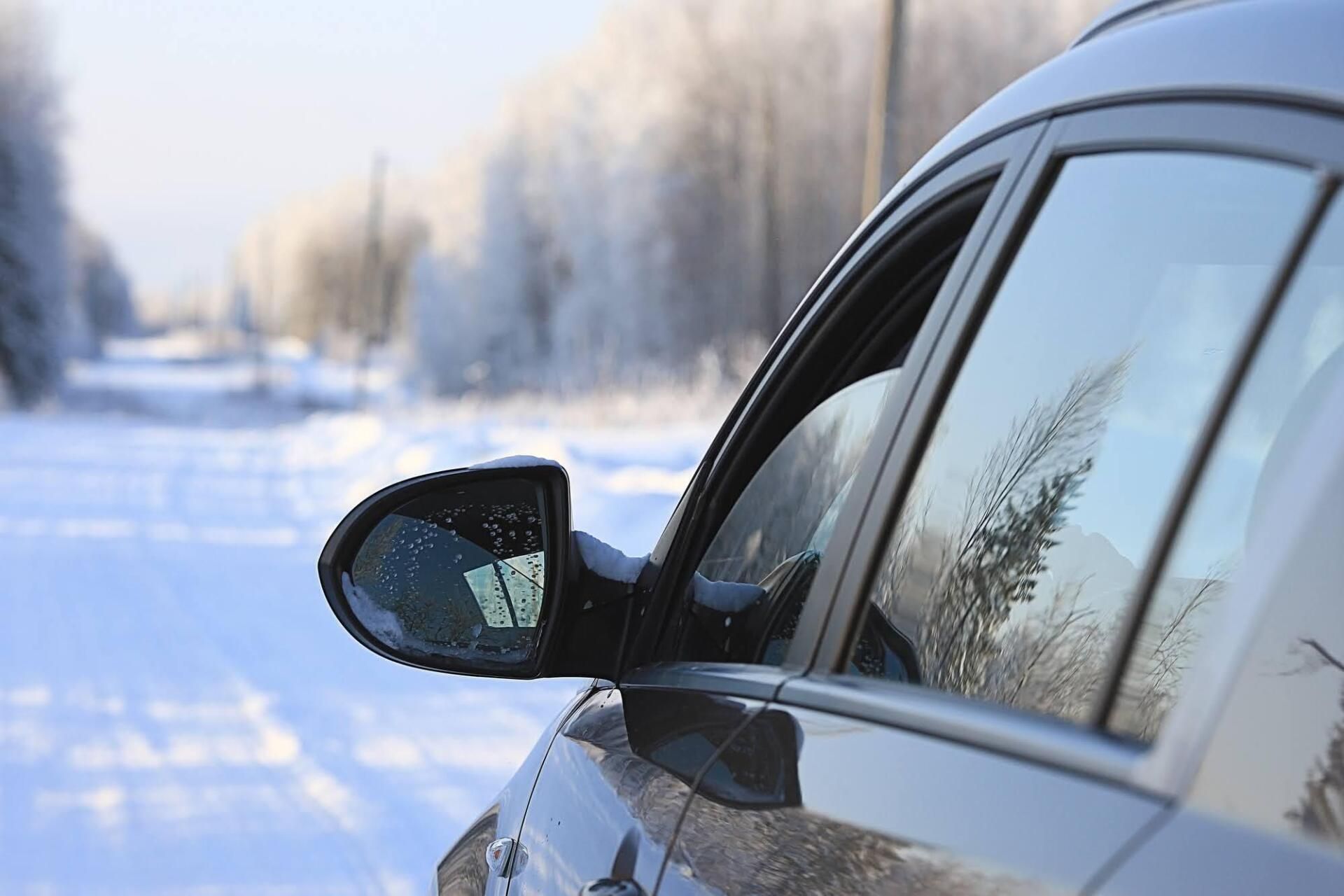 Car side mirror reflecting a snowy road and trees on a winter day