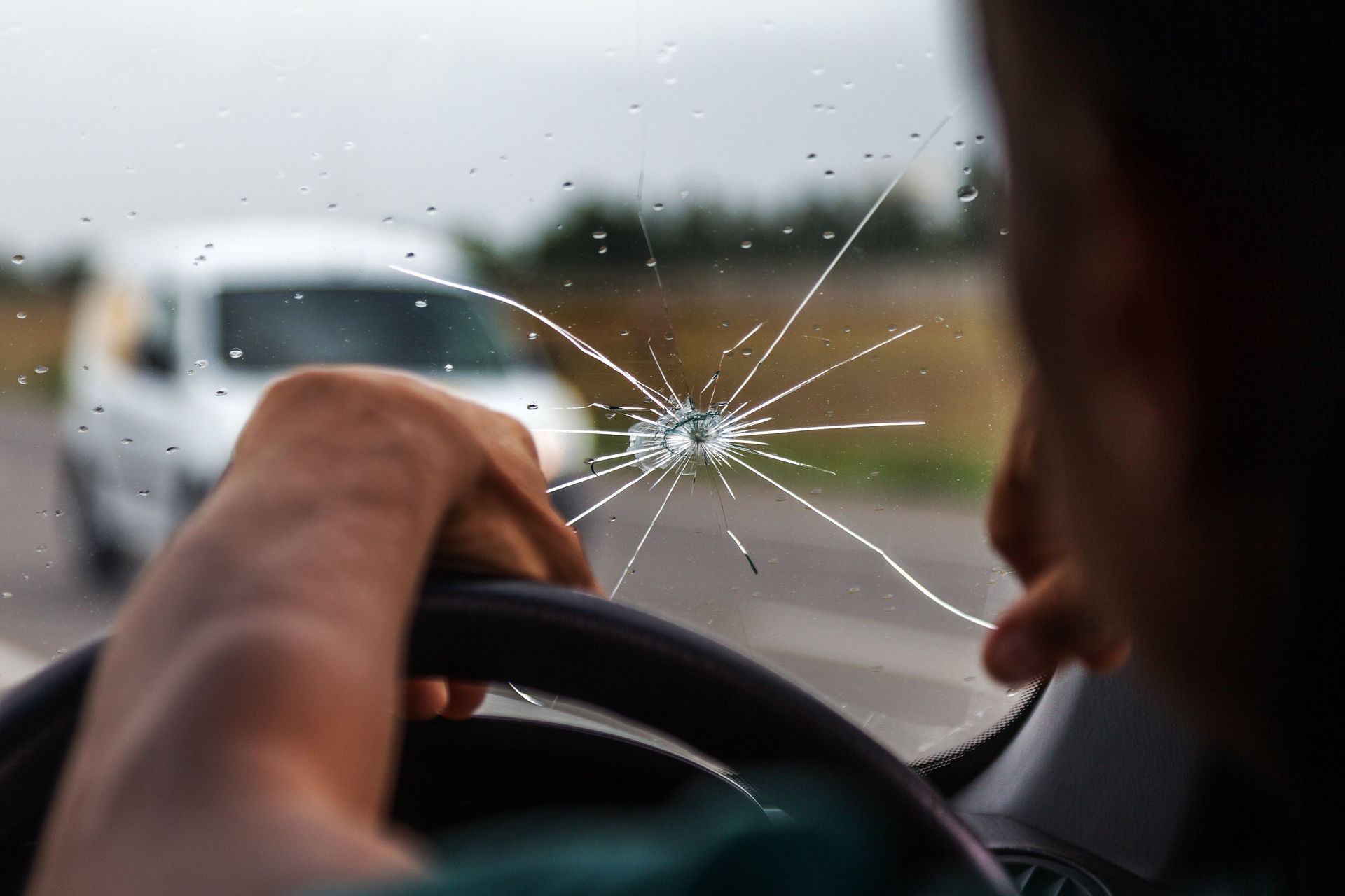 Driver holding steering wheel behind cracked windshield on a road