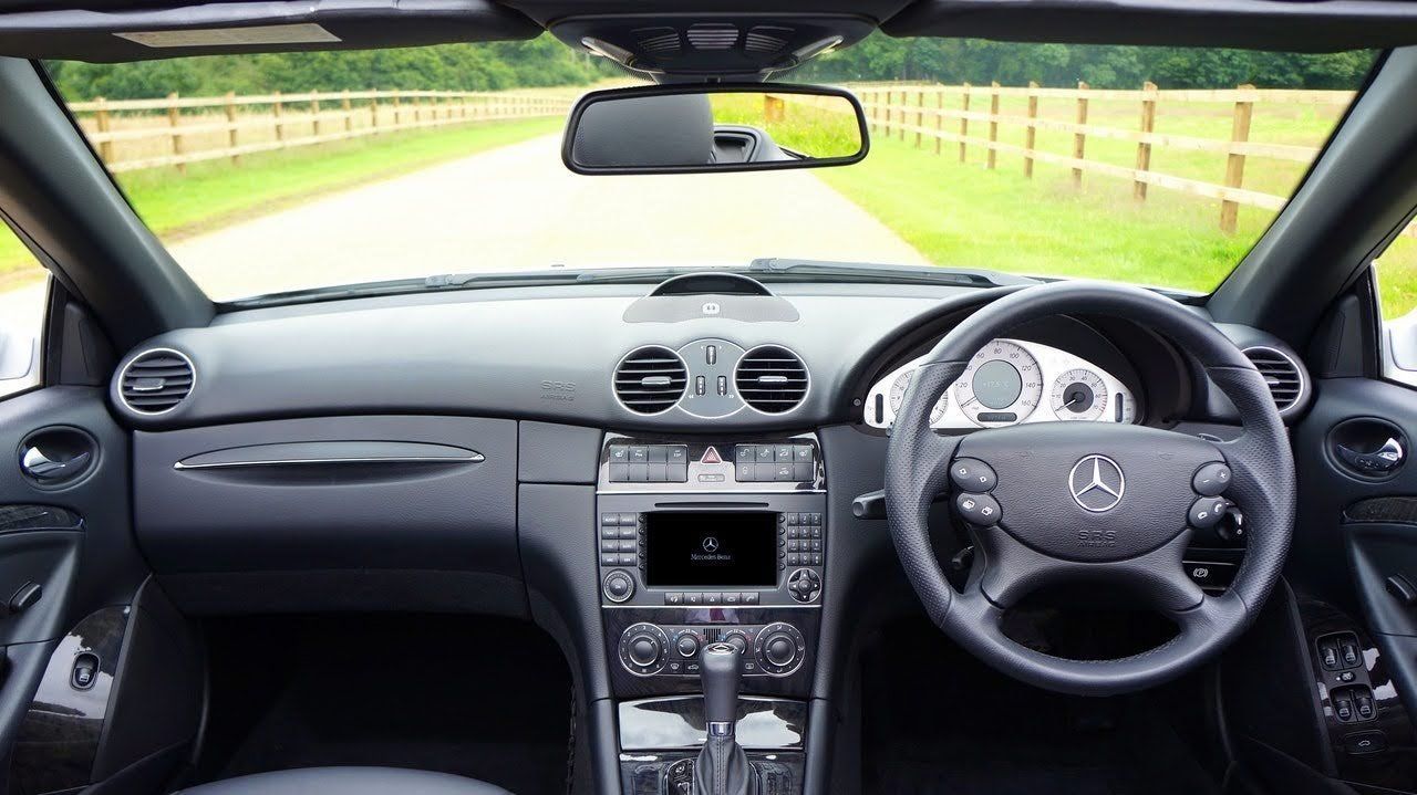 Car interior view from the driver’s seat, showing dashboard, steering wheel, and a road ahead through the windshield.