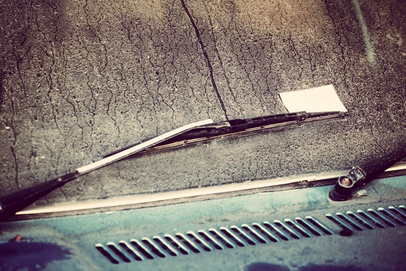 Windshield wiper resting on a car windshield, with a white card tucked under the blade.