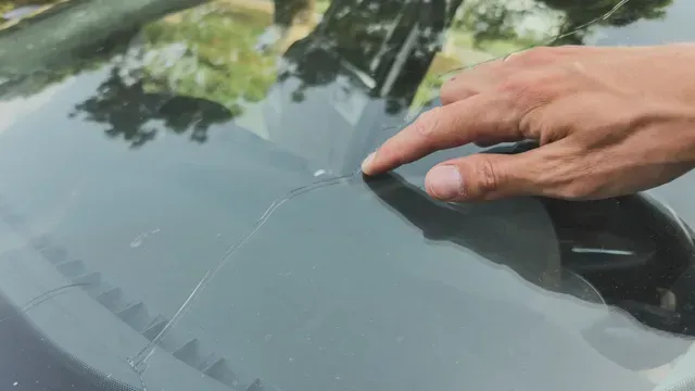 Hand pointing at a crack in a car windshield, outdoors.